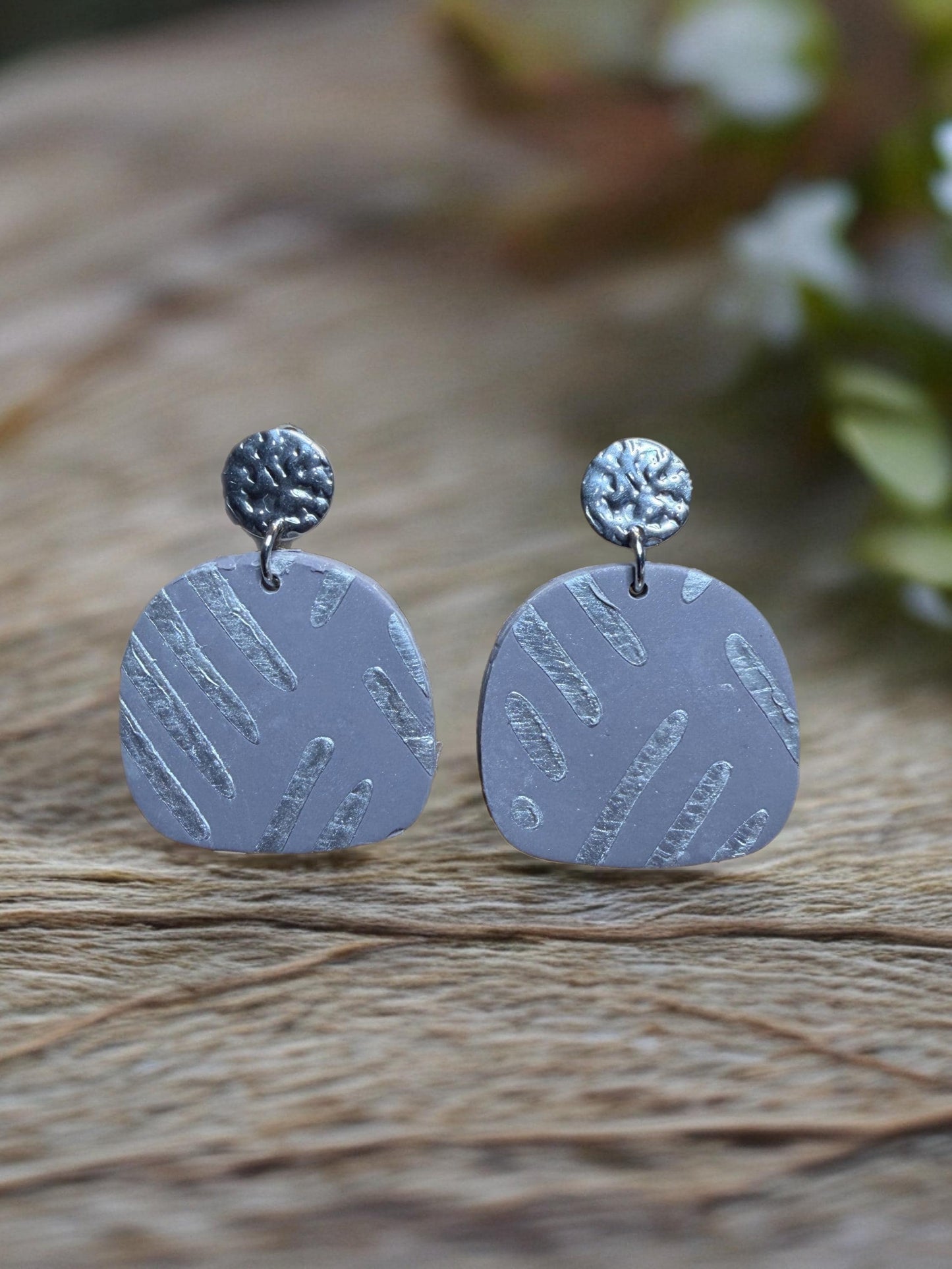 A pair of gray earrings with a metallic texture and circular designs on a wooden surface.