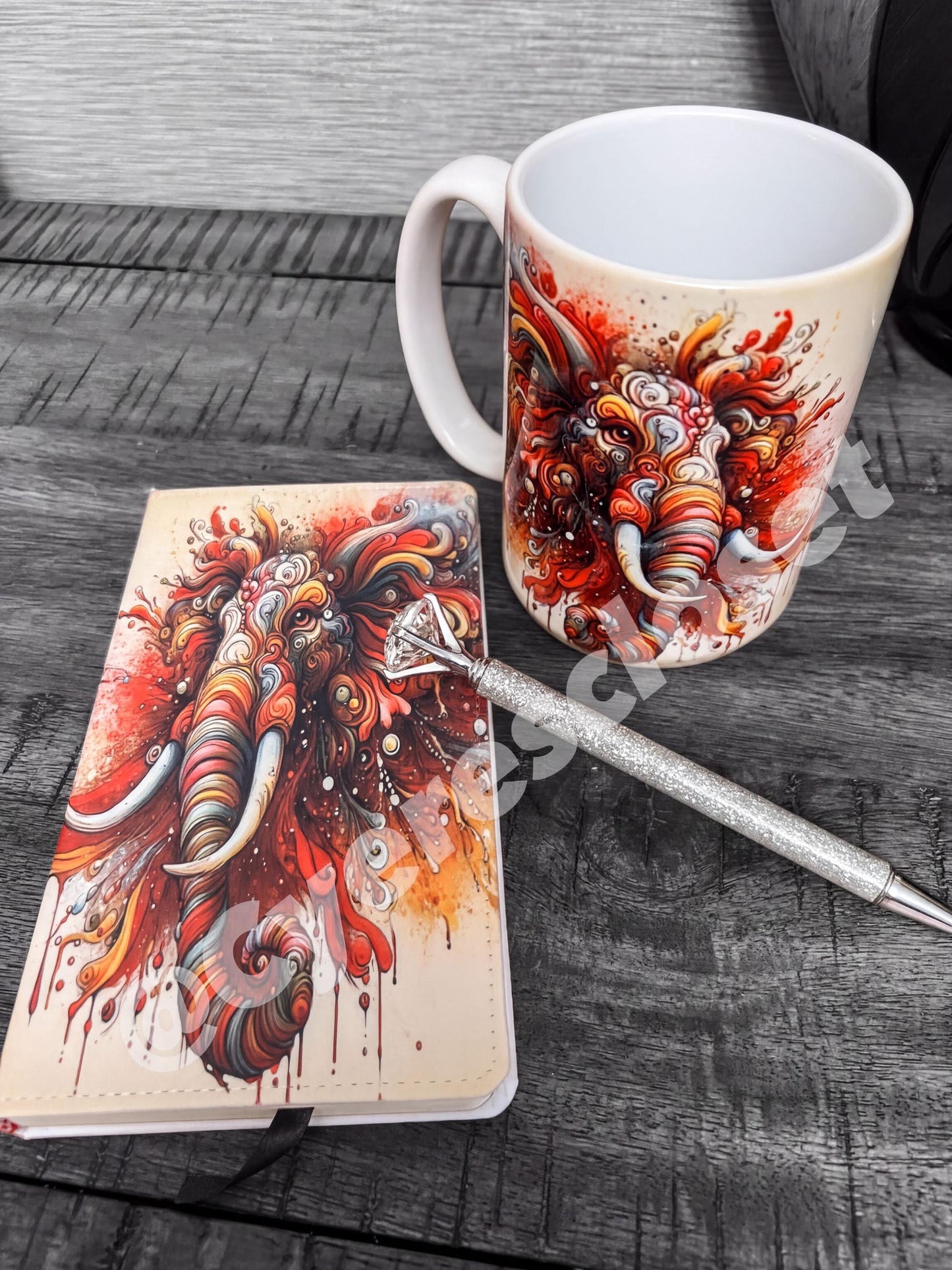 a white mug with a colorful elephant design, a notebook with a similar elephant design, and a pen on a wooden surface.