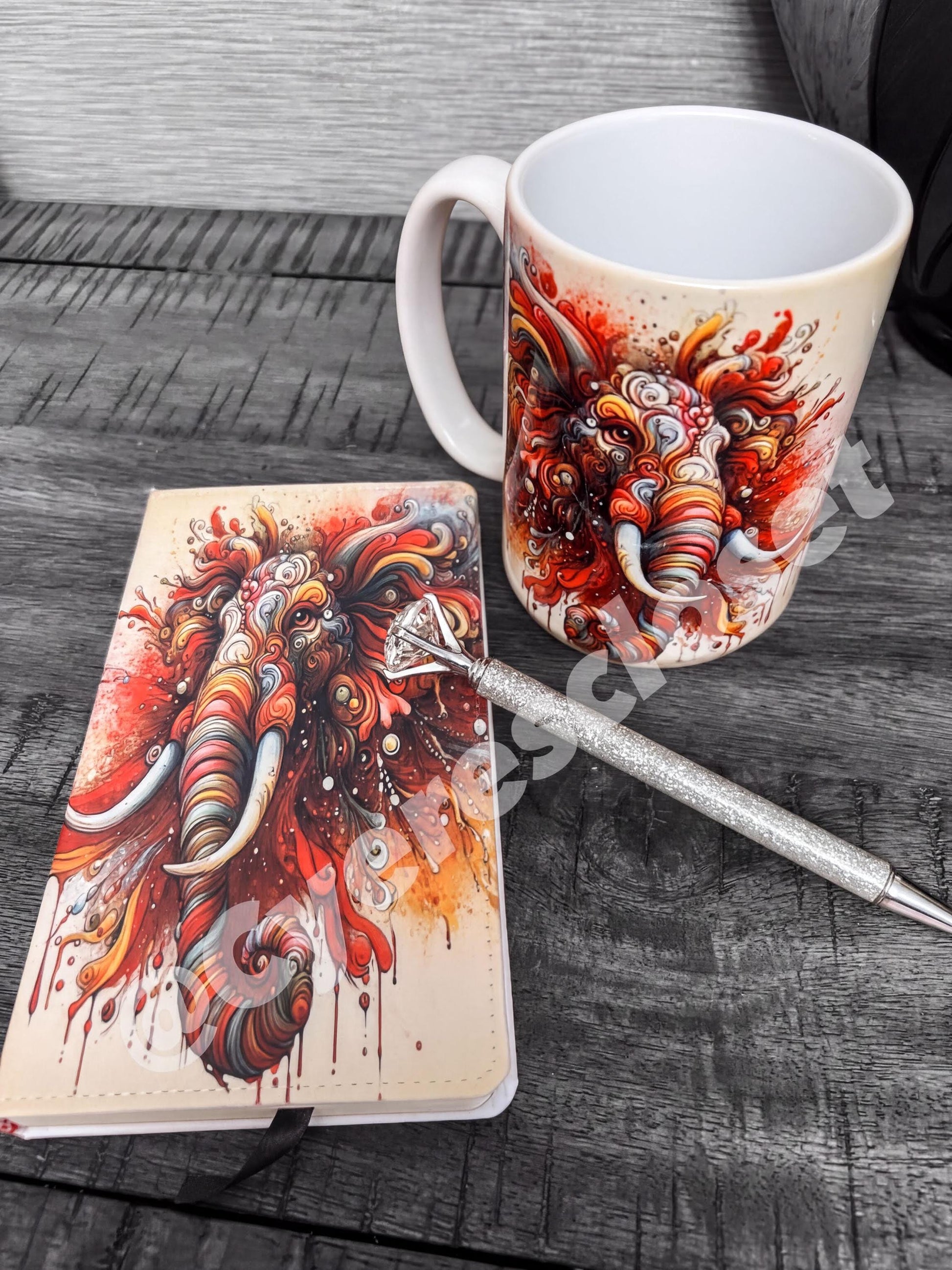 a white mug with a colorful elephant design, a notebook with a similar elephant design, and a pen on a wooden surface.