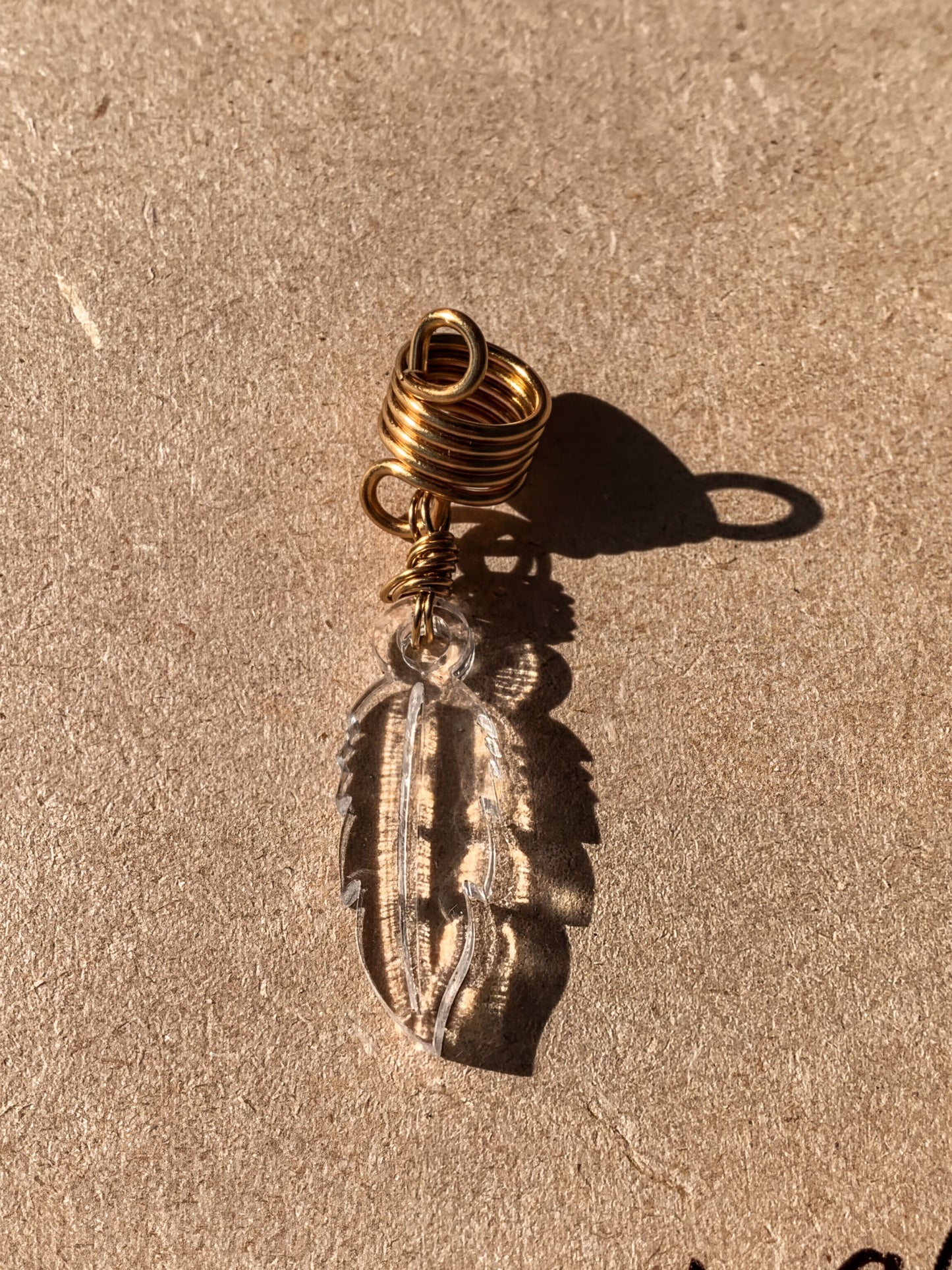 a clear glass feather pendant with a gold spiral design, hanging on a brown surface.