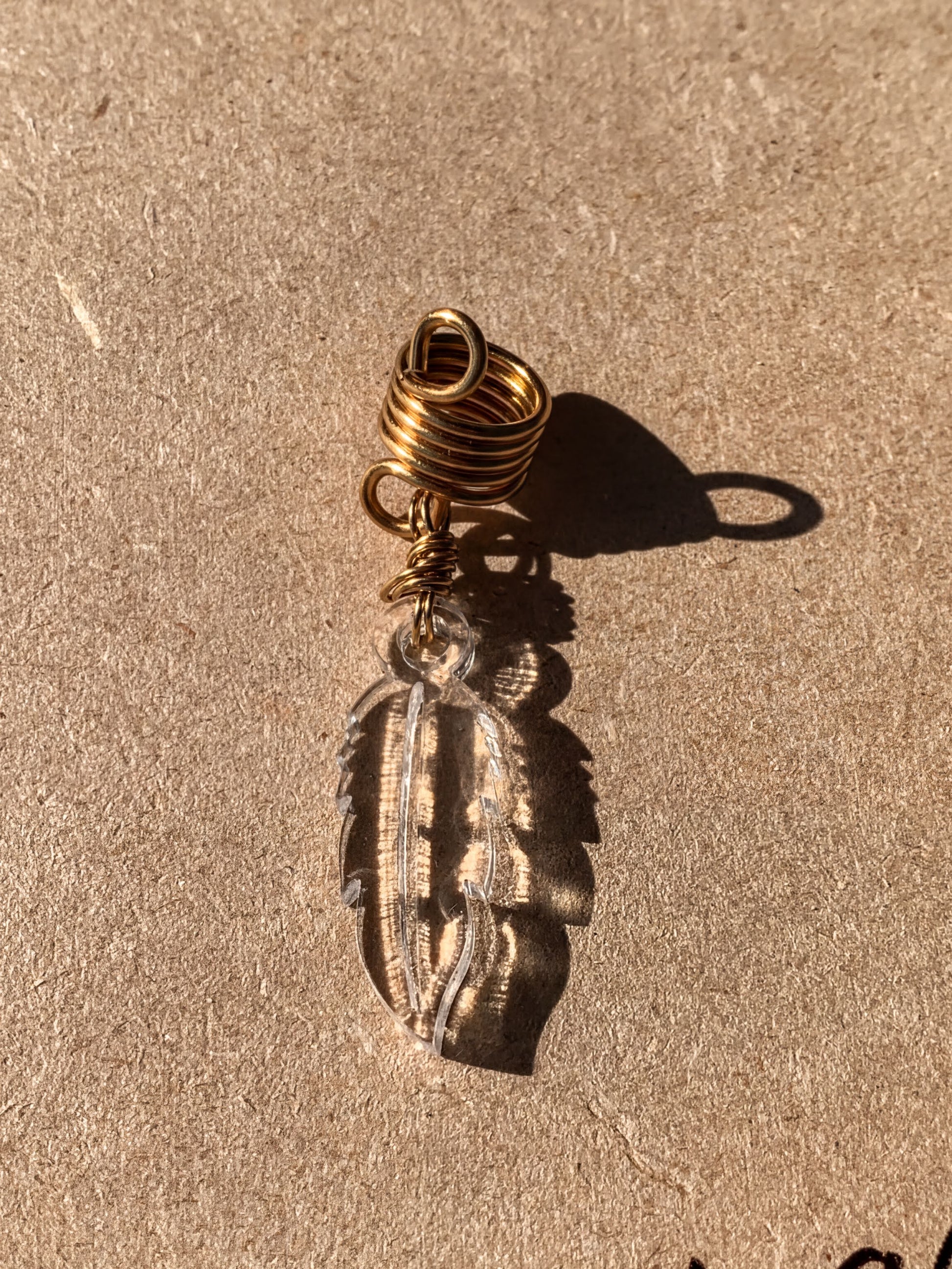 a clear glass feather pendant with a gold spiral design, hanging on a brown surface.