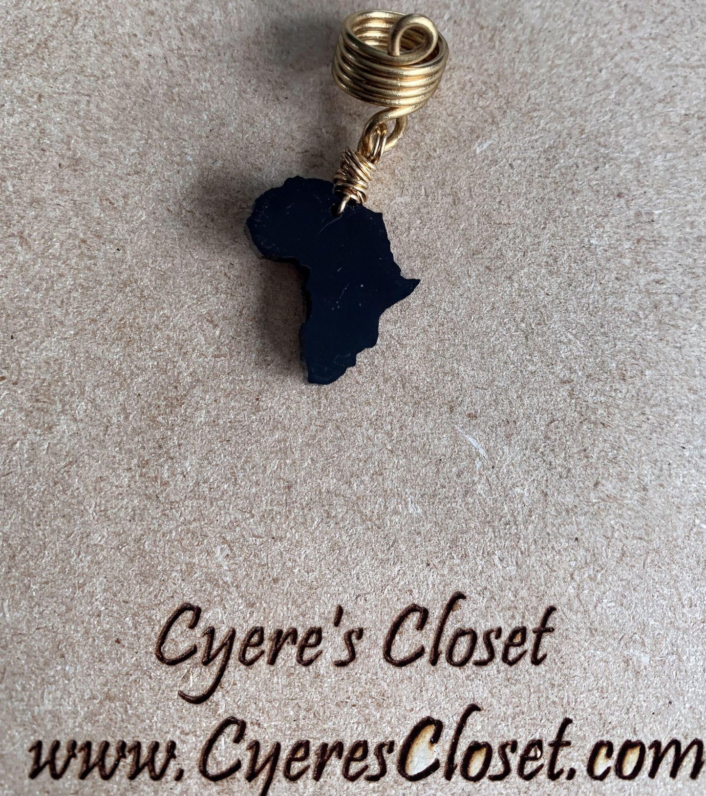 a black African continent pendant with a gold loop, placed on a brown surface.