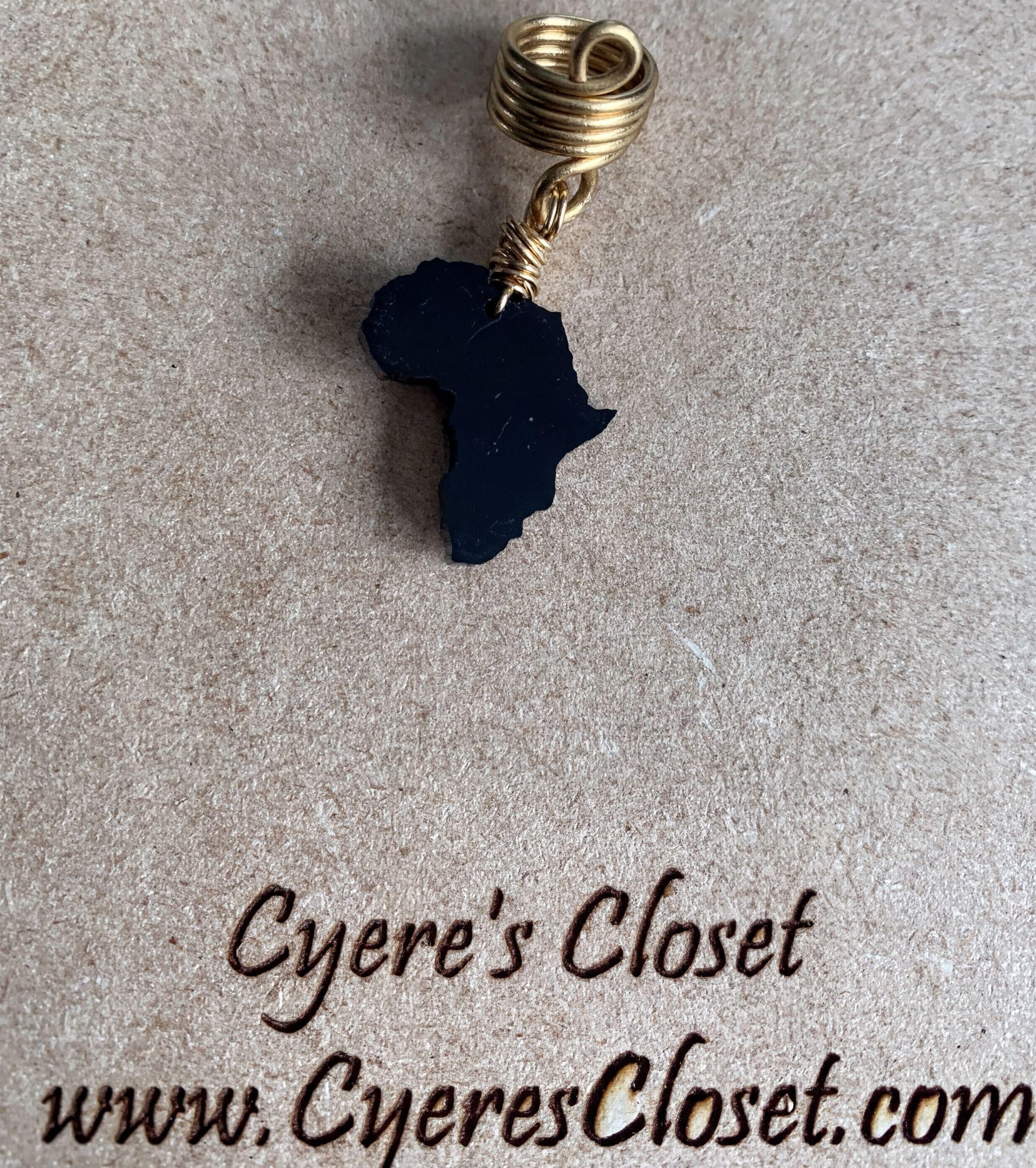 a black African continent pendant with a gold loop, placed on a brown surface.