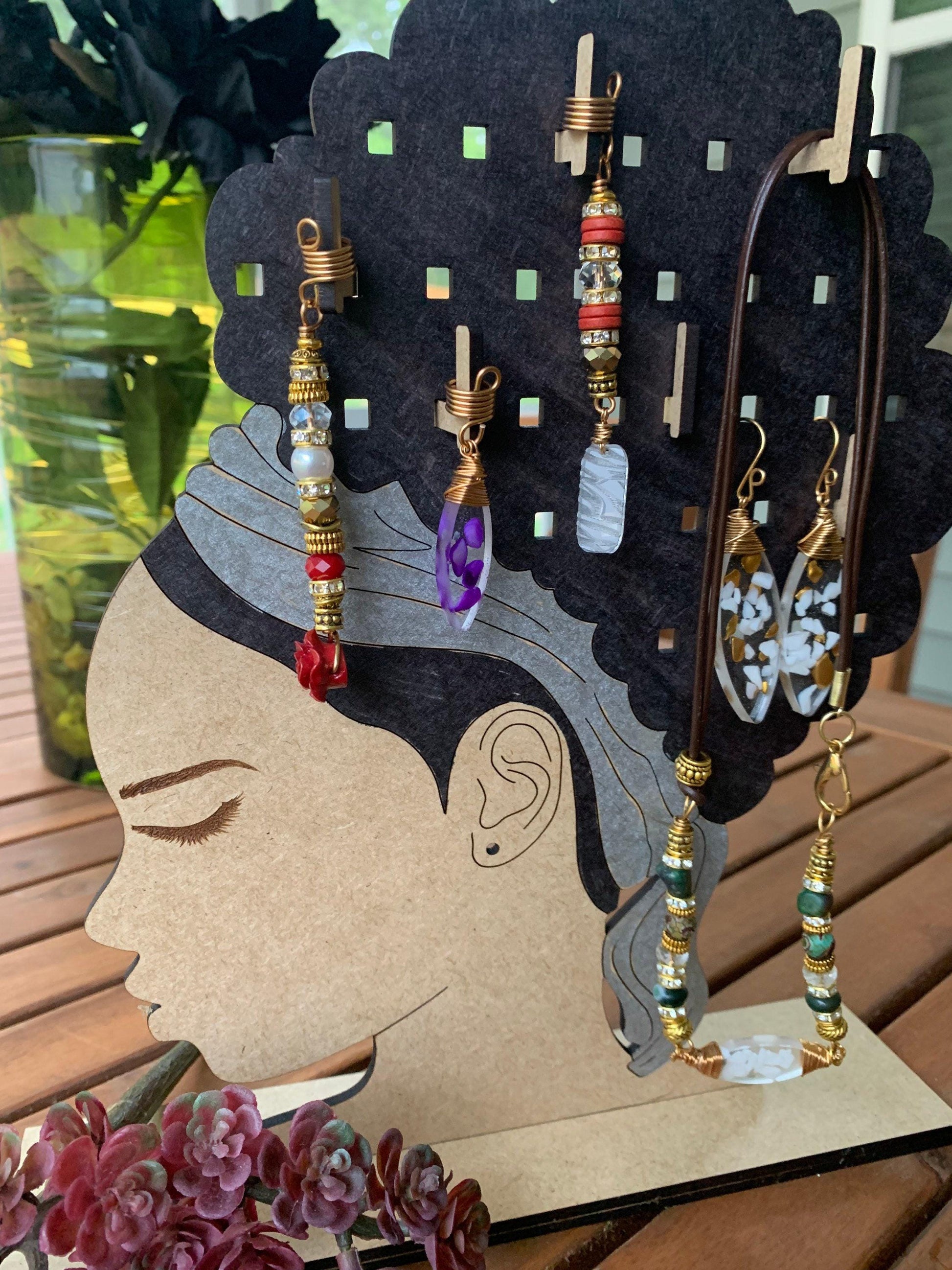 A wooden jewelry stand displaying various earrings and necklaces, with a vase of flowers in the background.