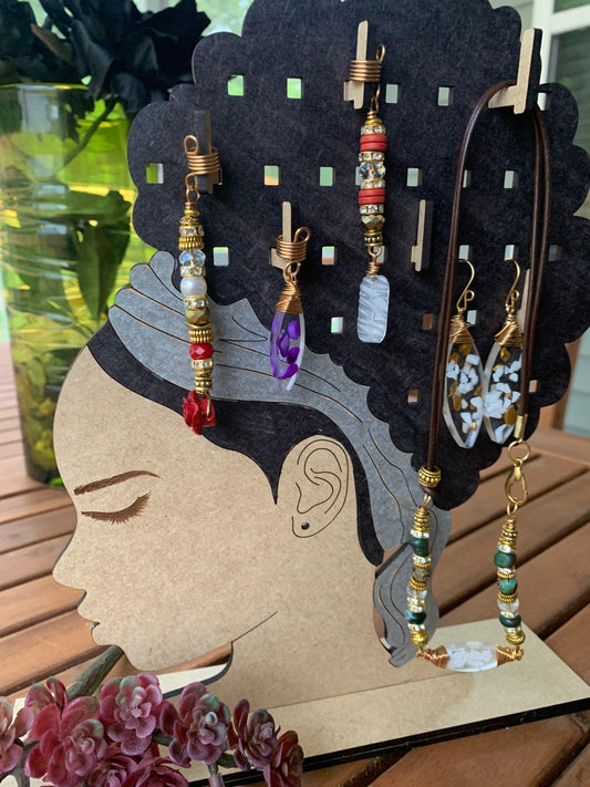 A wooden jewelry stand displaying various earrings and necklaces, with a vase of flowers in the background.