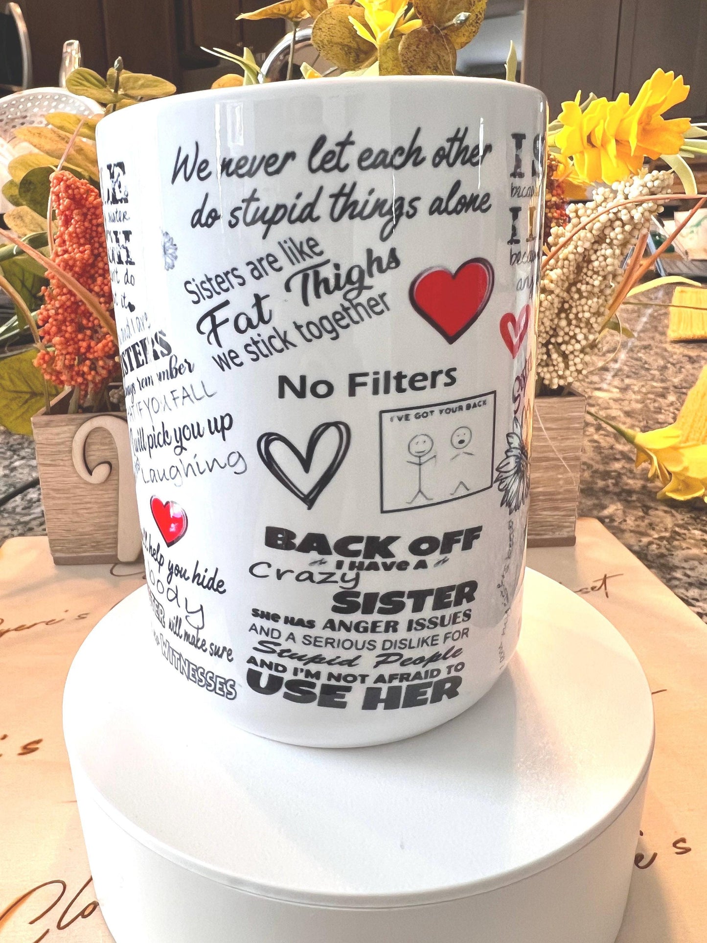 a white mug with various phrases and sayings printed on it, placed on a table with yellow flowers in the background.