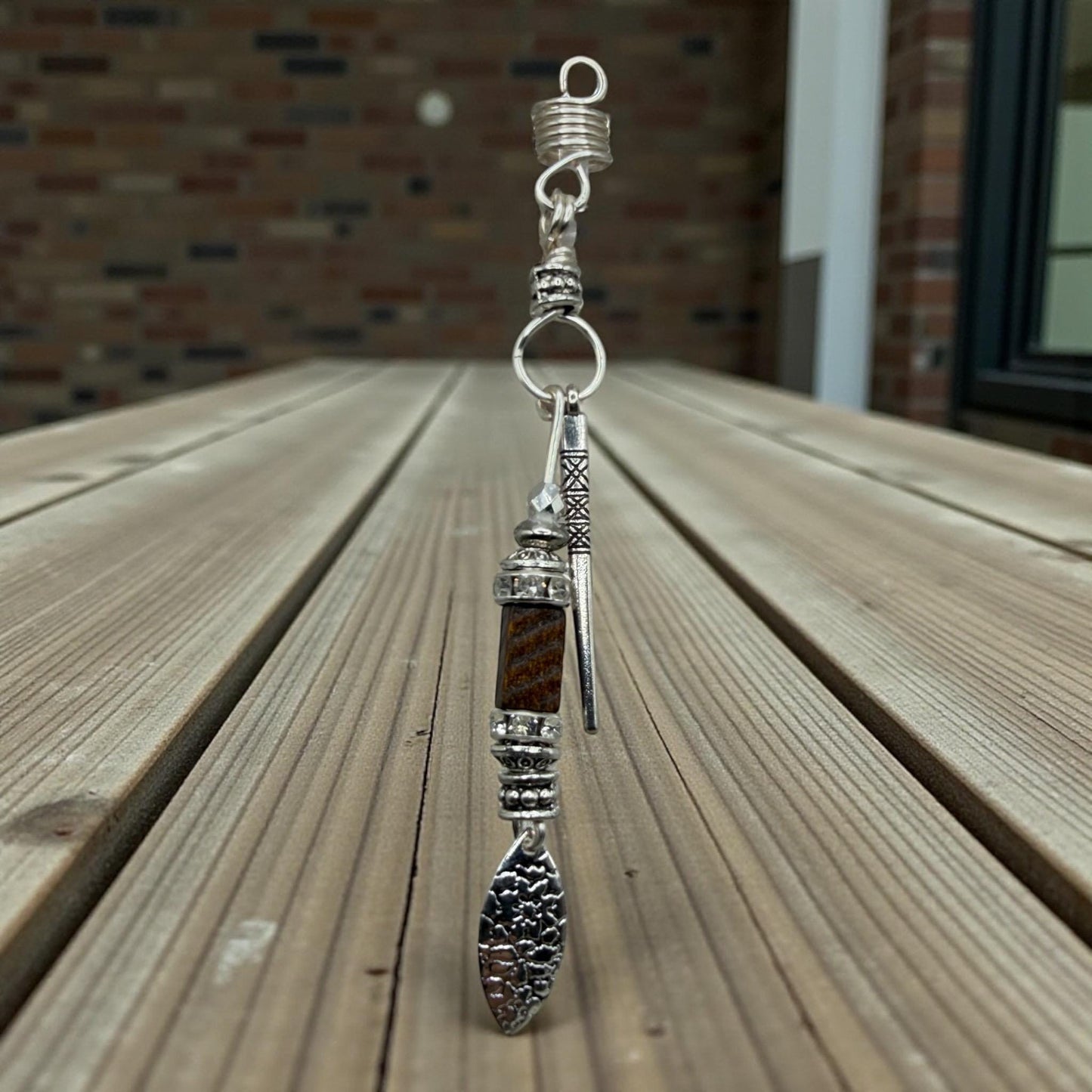 A silver-colored metal pendant with a decorative design hangs from a hook on a wooden surface.