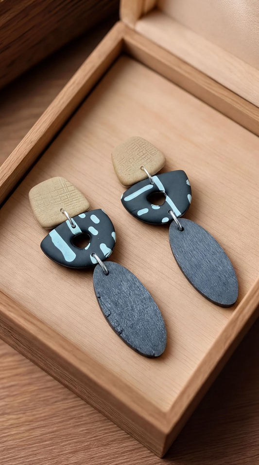 A pair of earrings with a combination of black and blue colors, featuring a wooden box as the display.