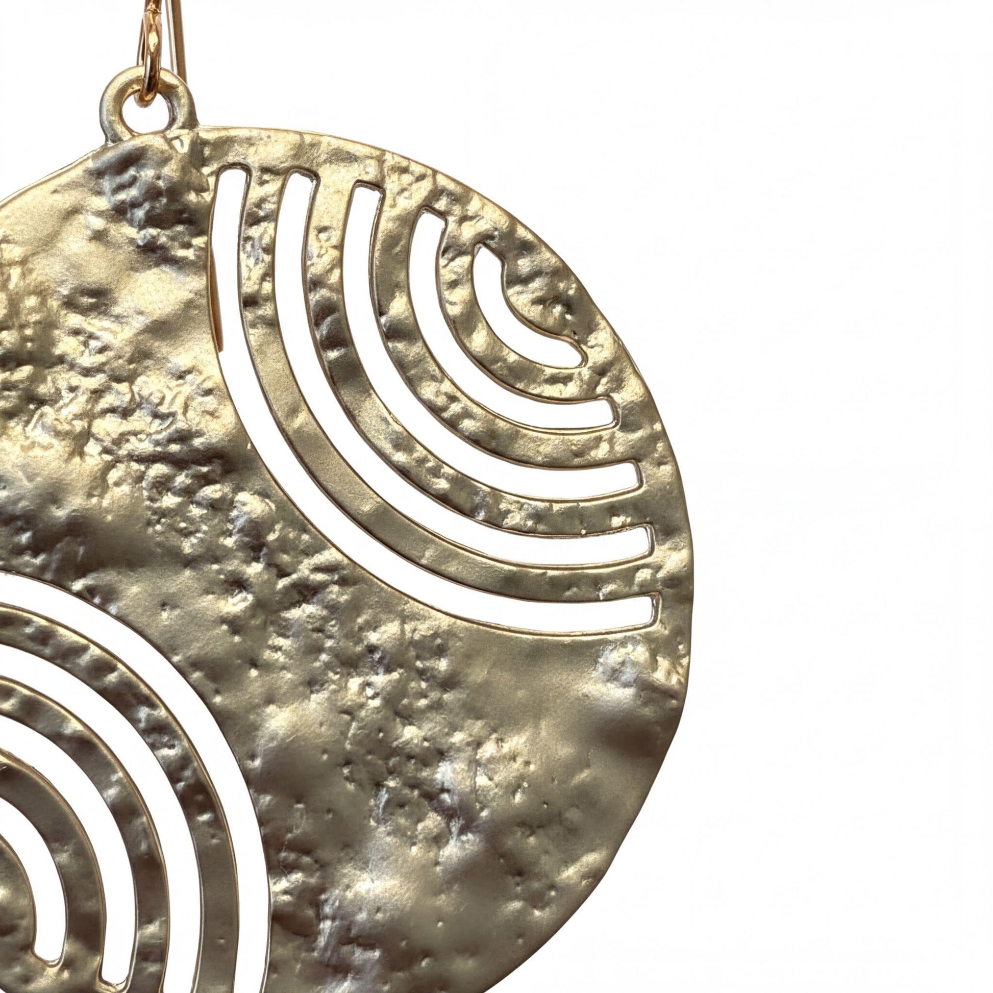 A close-up view of a gold-colored metal earring with a circular cutout design featuring concentric circles and a wave-like pattern.