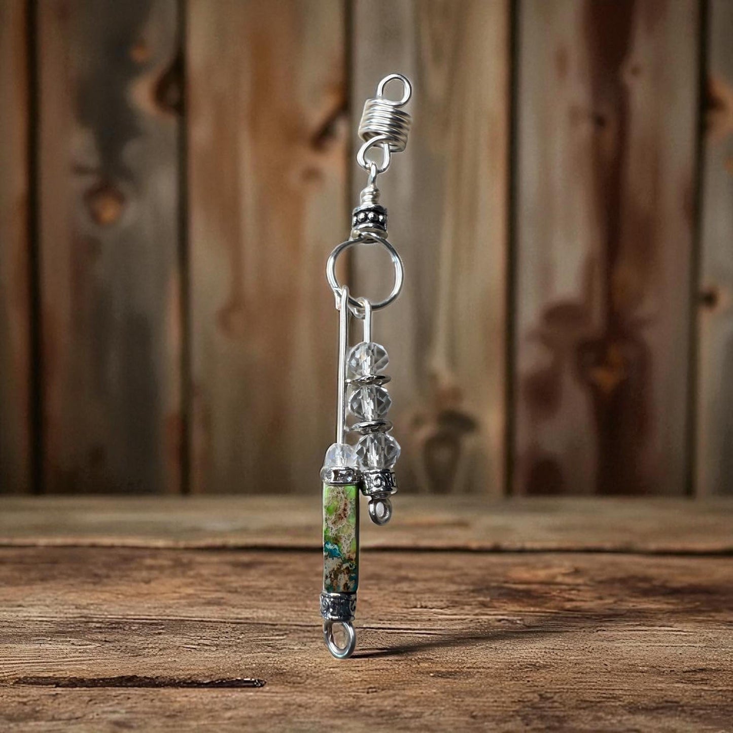 A silver-colored pendant with a clear glass bead and a metal clasp is displayed on a wooden surface against a wooden background.