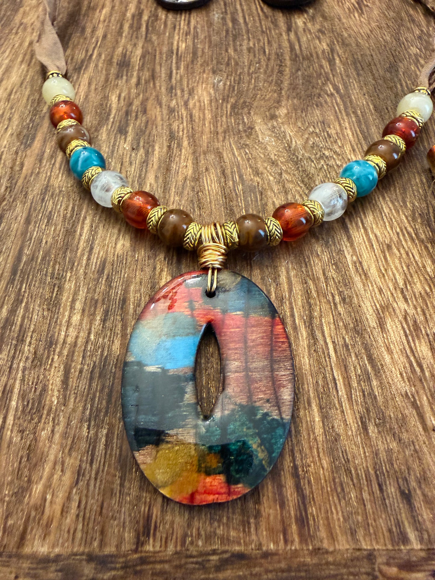 A colorful pendant necklace with a large oval-shaped pendant featuring a vibrant abstract design in various colors.