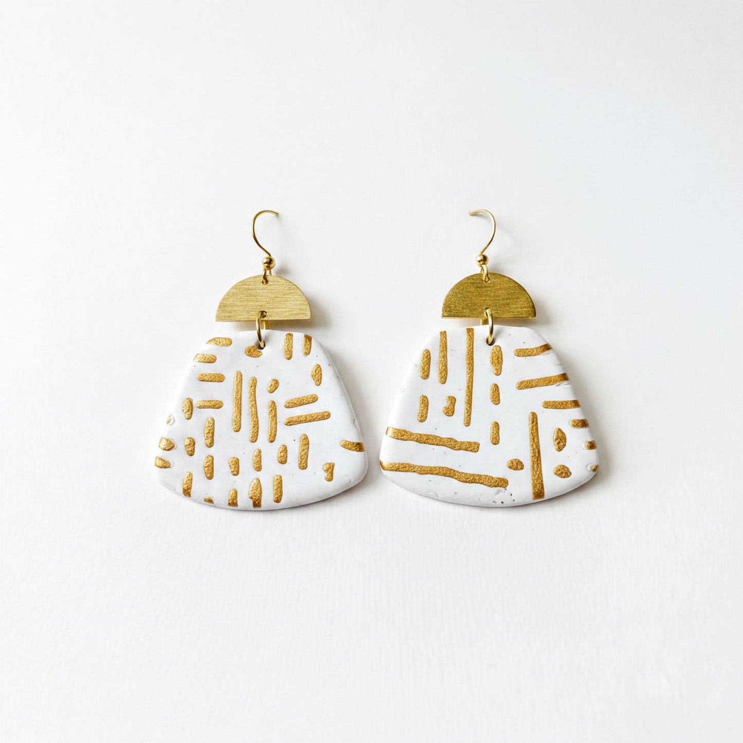 A pair of white earrings with gold stripes and a geometric pattern, displayed against a white background.