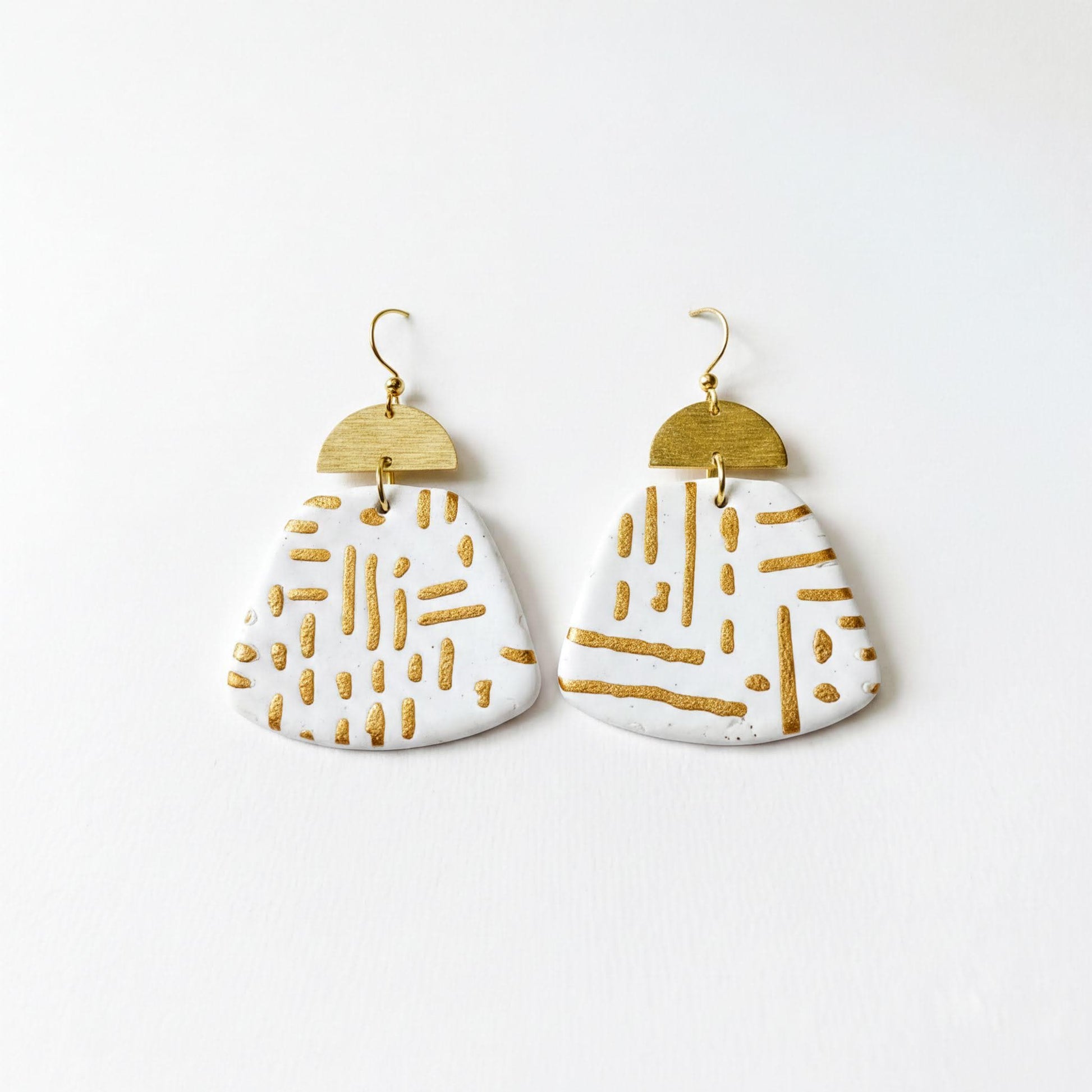 A pair of white earrings with gold stripes and a geometric pattern, displayed against a white background.