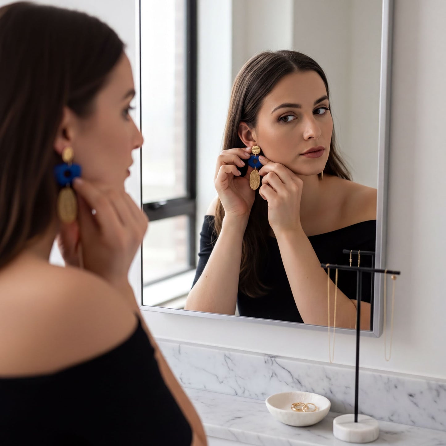 A woman is seen in front of a mirror, adjusting her earrings.