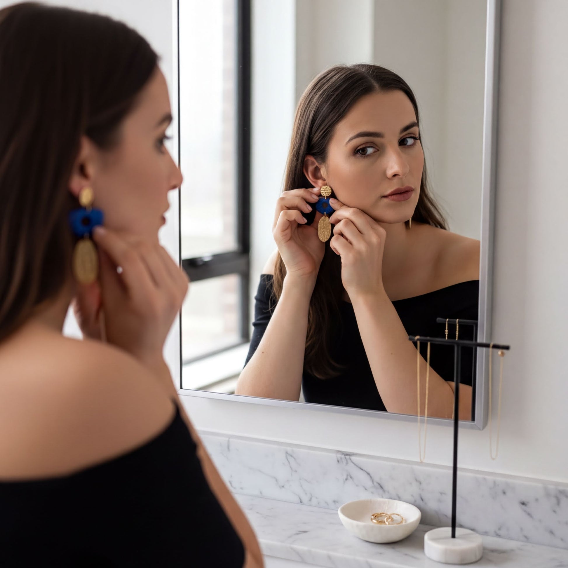 A woman is seen in front of a mirror, adjusting her earrings.