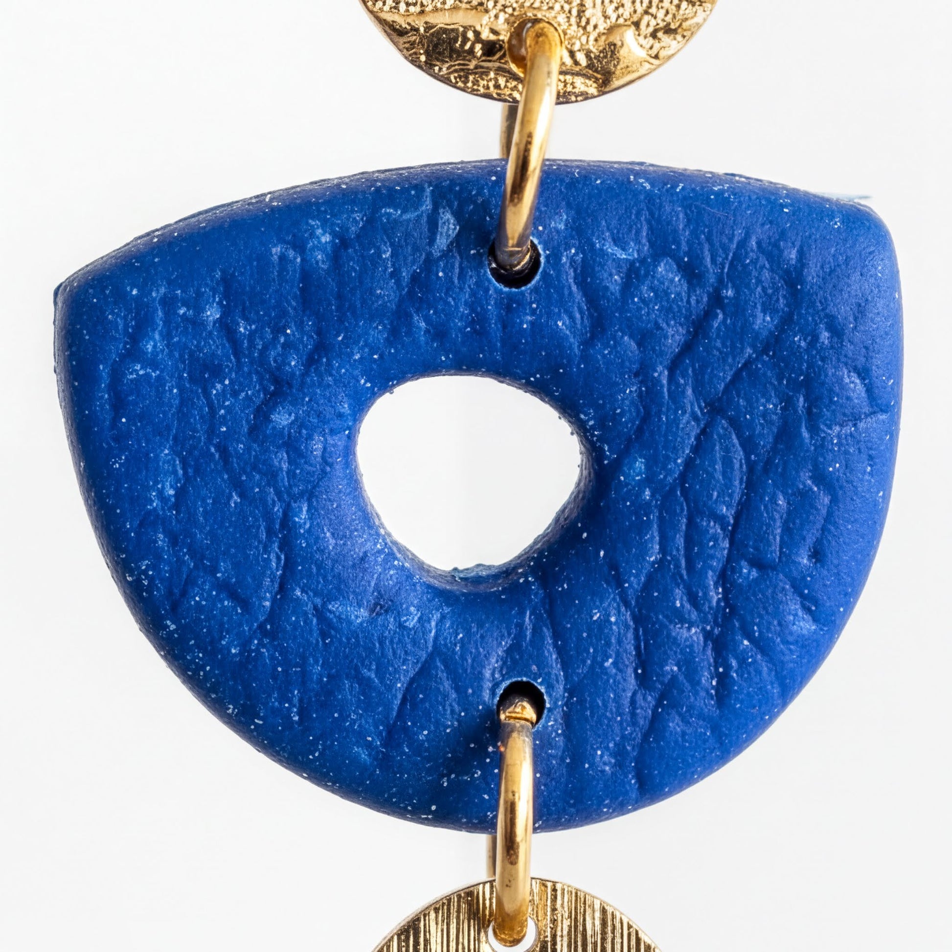 A close-up image of a blue, textured pendant with a hole in the center, hanging from a gold-colored metal hook.