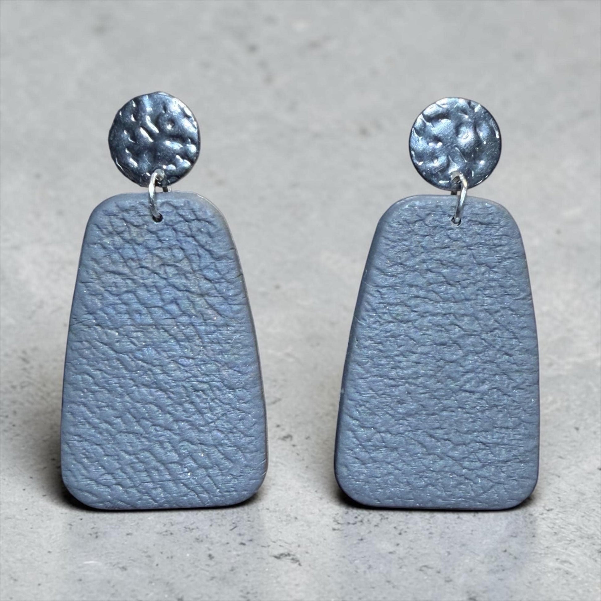 A pair of gray, textured earrings with metal circular elements on top.