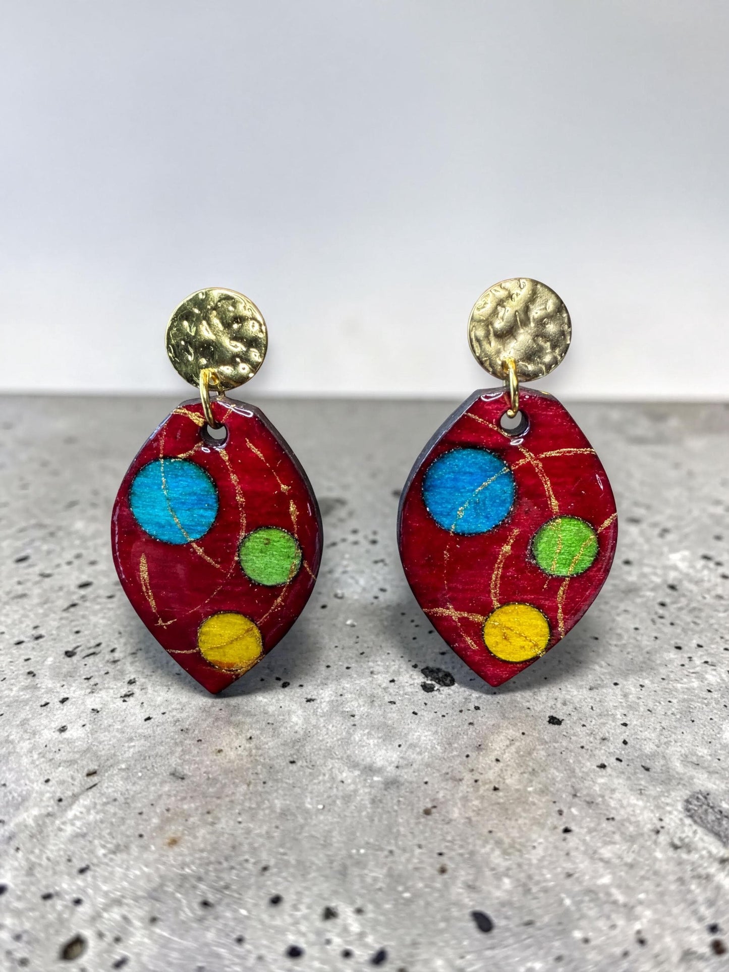A pair of red earrings with colorful polka dots and gold-colored metal accents.