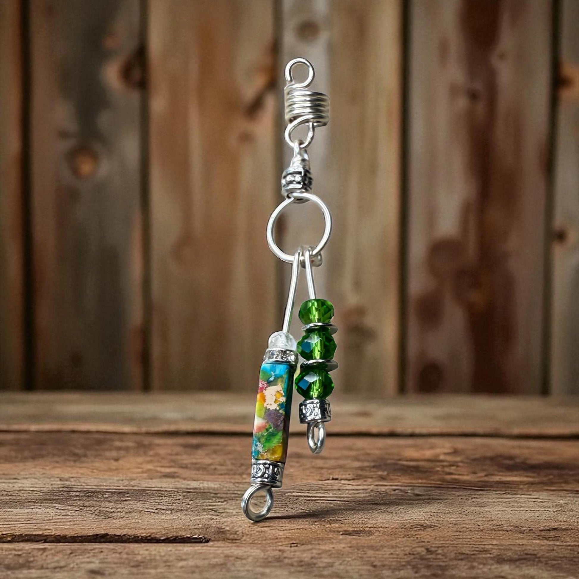 A silver necklace with colorful beads and a spring-like clasp is displayed on a wooden surface against a wooden background.