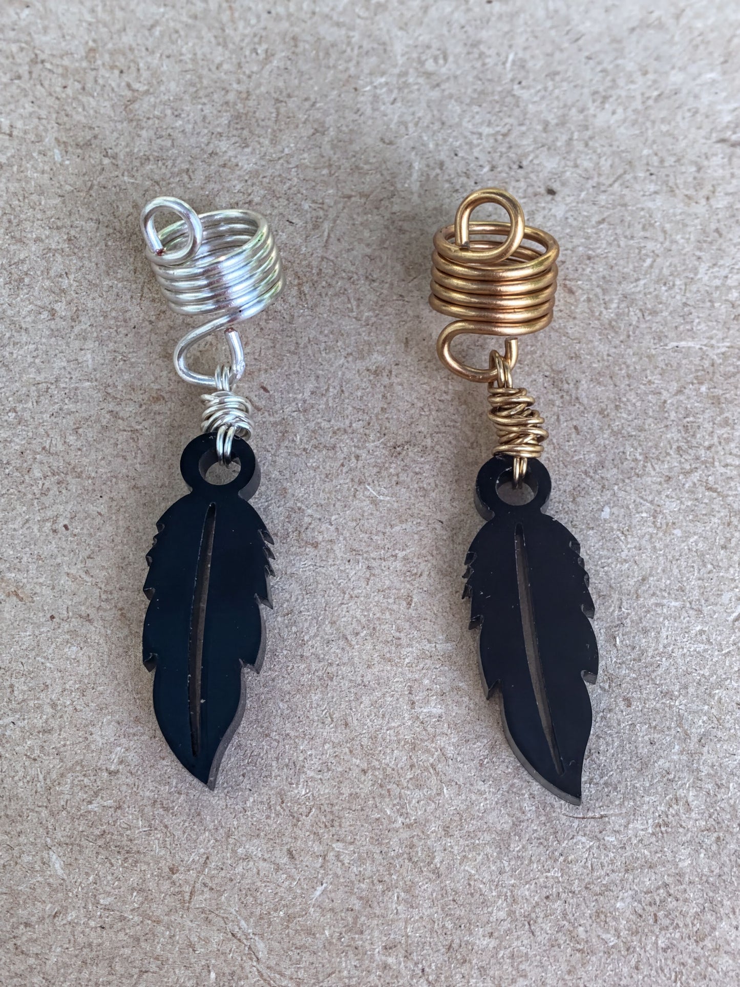 two pairs of earrings, each with a feather-shaped pendant. The earrings are made of metal and have a spiral design on the top.