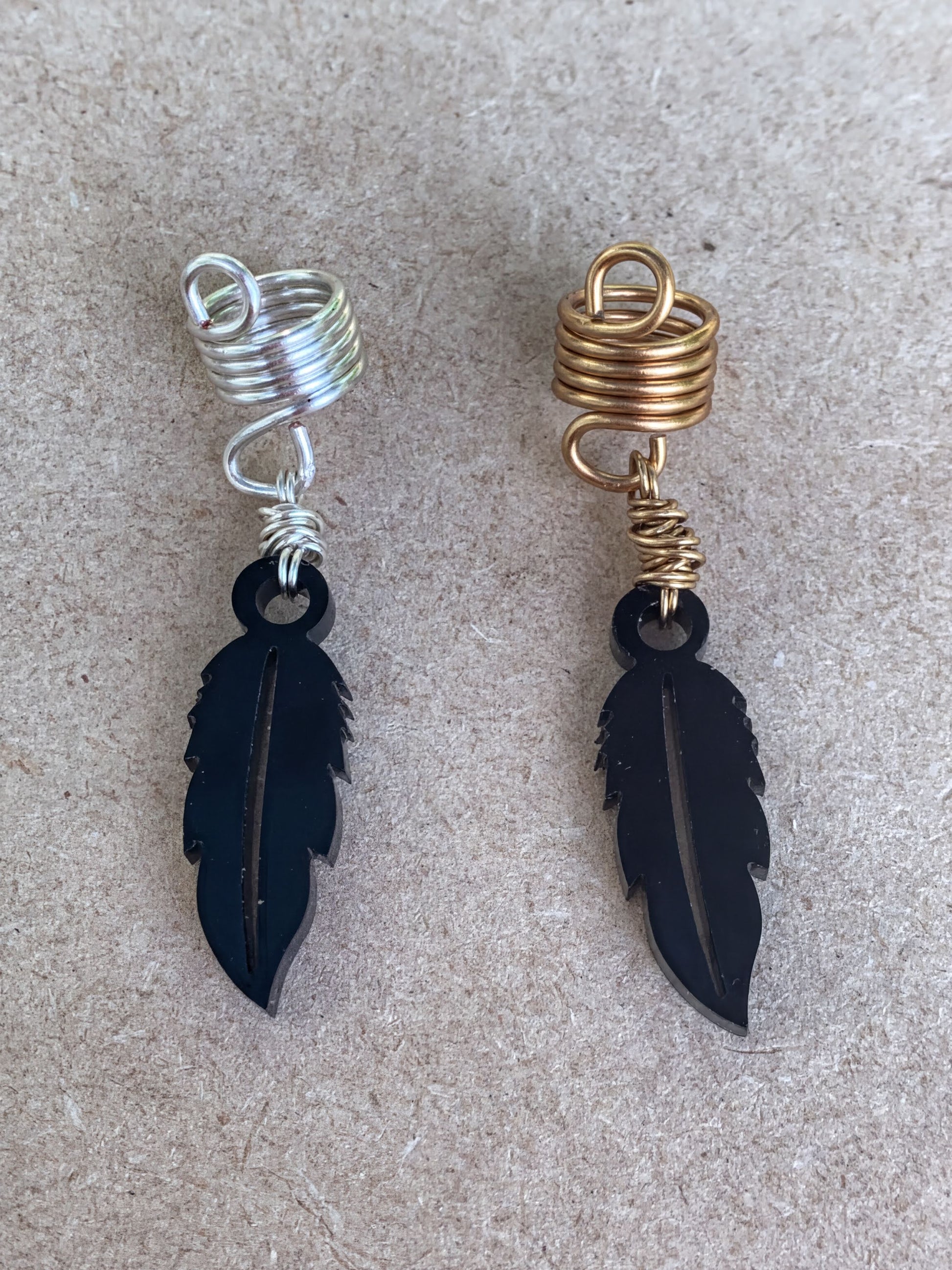 two pairs of earrings, each with a feather-shaped pendant. The earrings are made of metal and have a spiral design on the top.