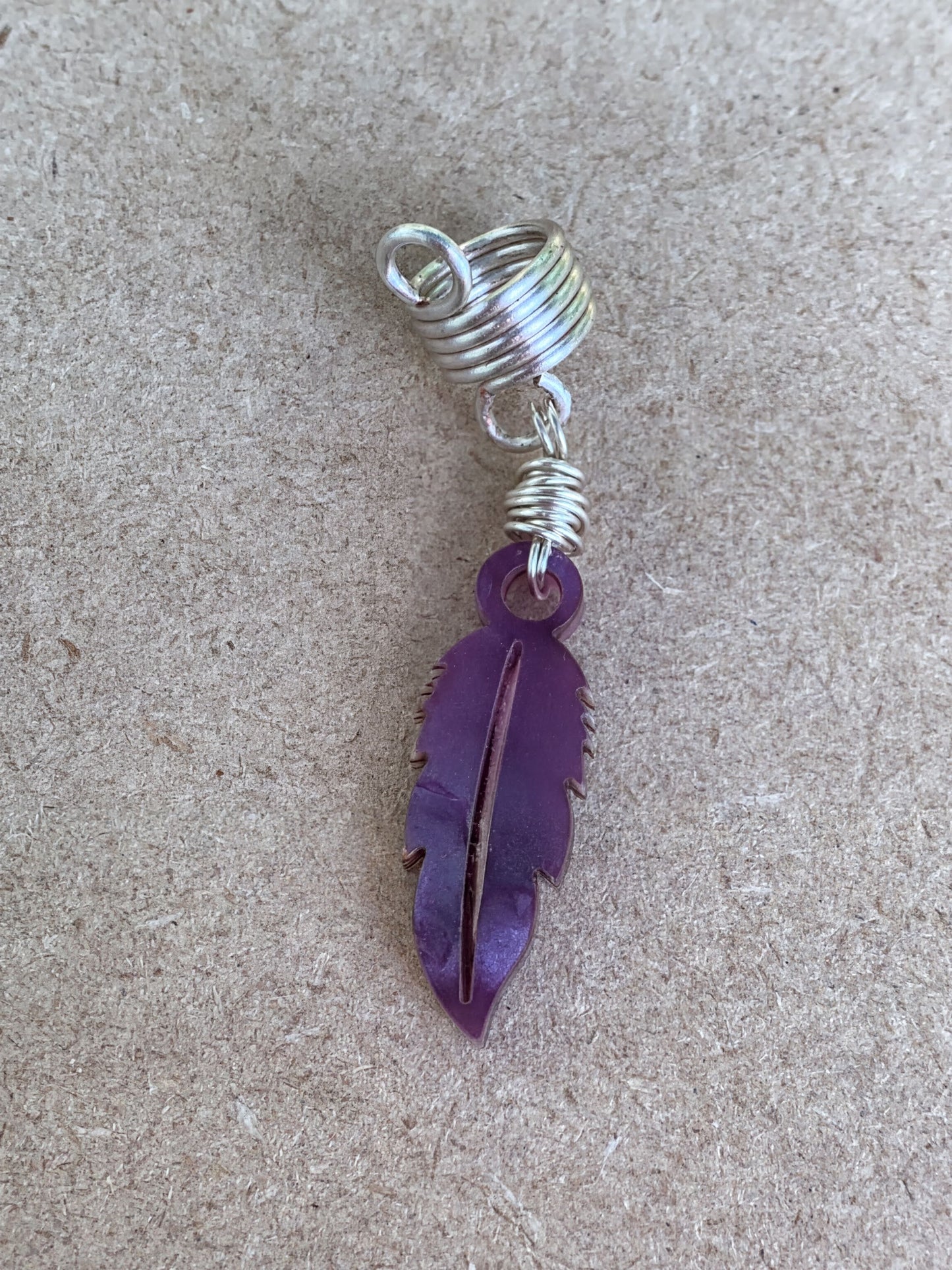 A purple feather earring with a spiral design is shown against a textured background.