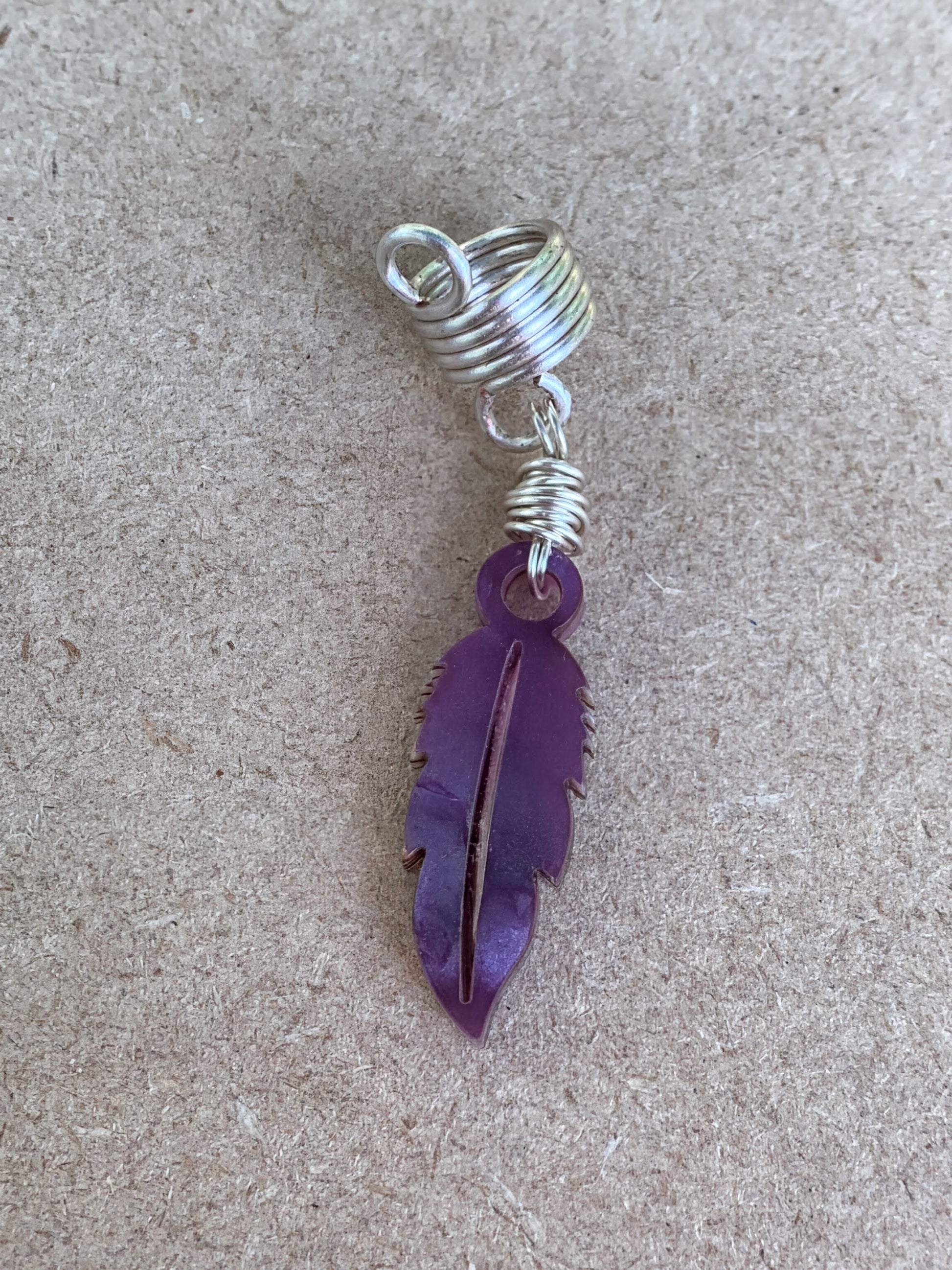 A purple feather earring with a spiral design is shown against a textured background.
