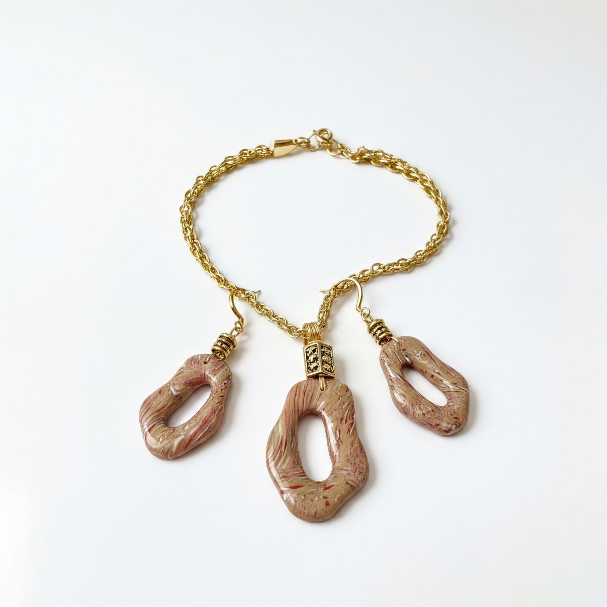 A gold-colored necklace with three pendants, each featuring a unique, irregular shape and a metallic finish.