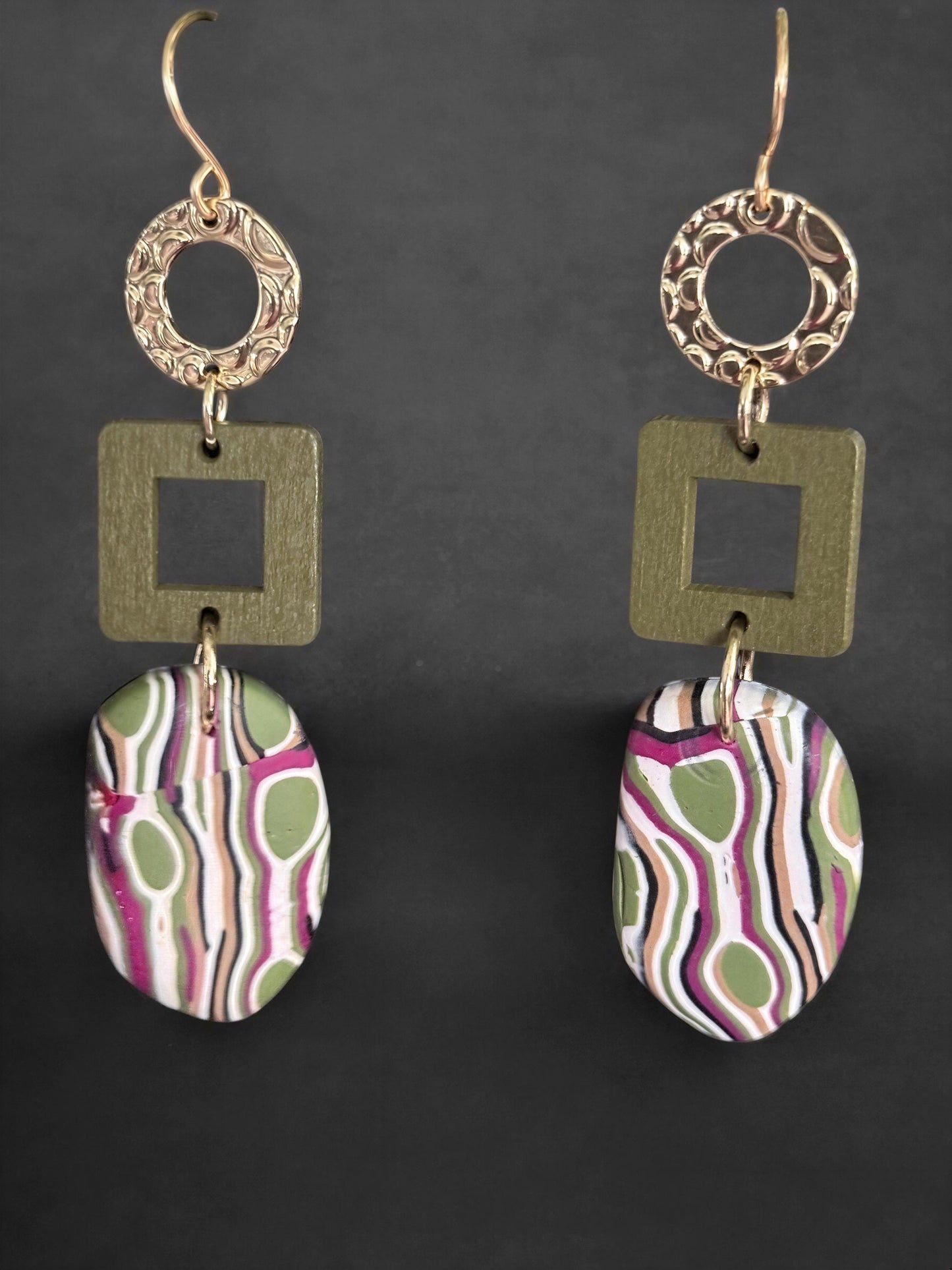 a pair of earrings with a unique design featuring a combination of geometric shapes and abstract patterns in various colors, including green, pink, and white.
