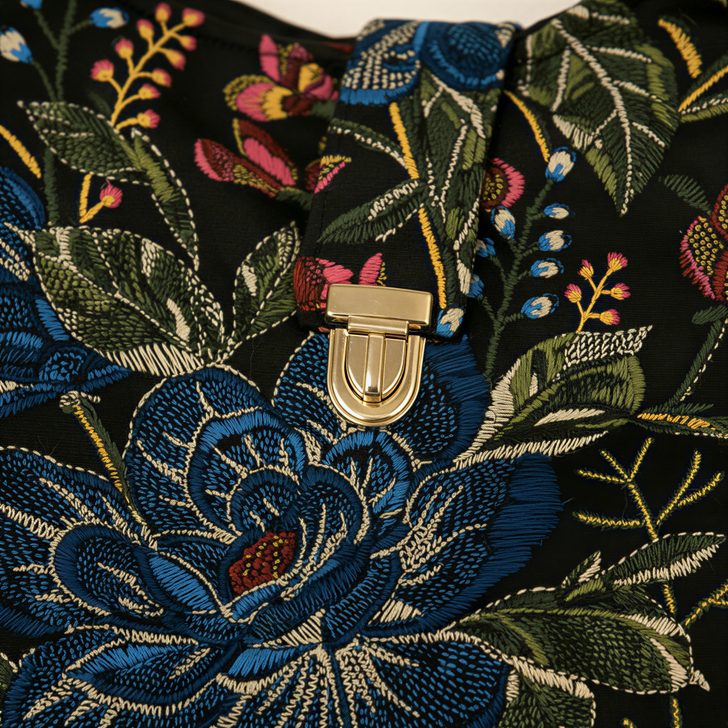 a close-up view of a black fabric with a vibrant floral pattern, featuring a gold clasp on the front.