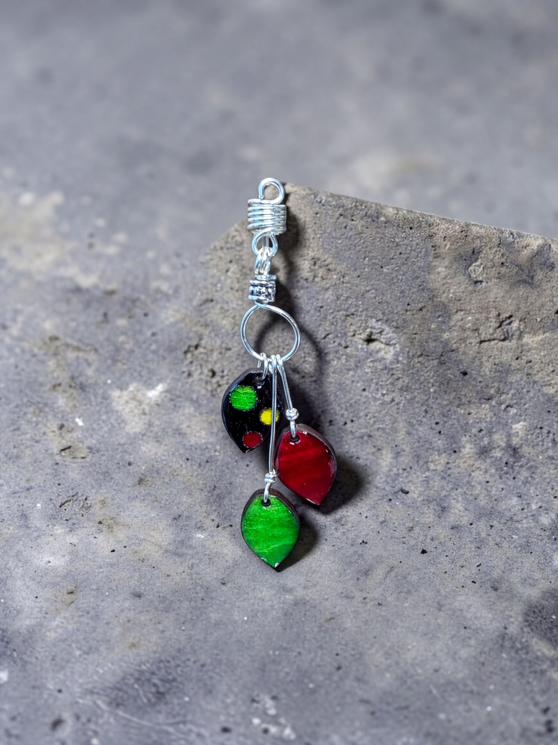 A colorful earring with a metal hook and three leaf-shaped charms in red, green, and black.