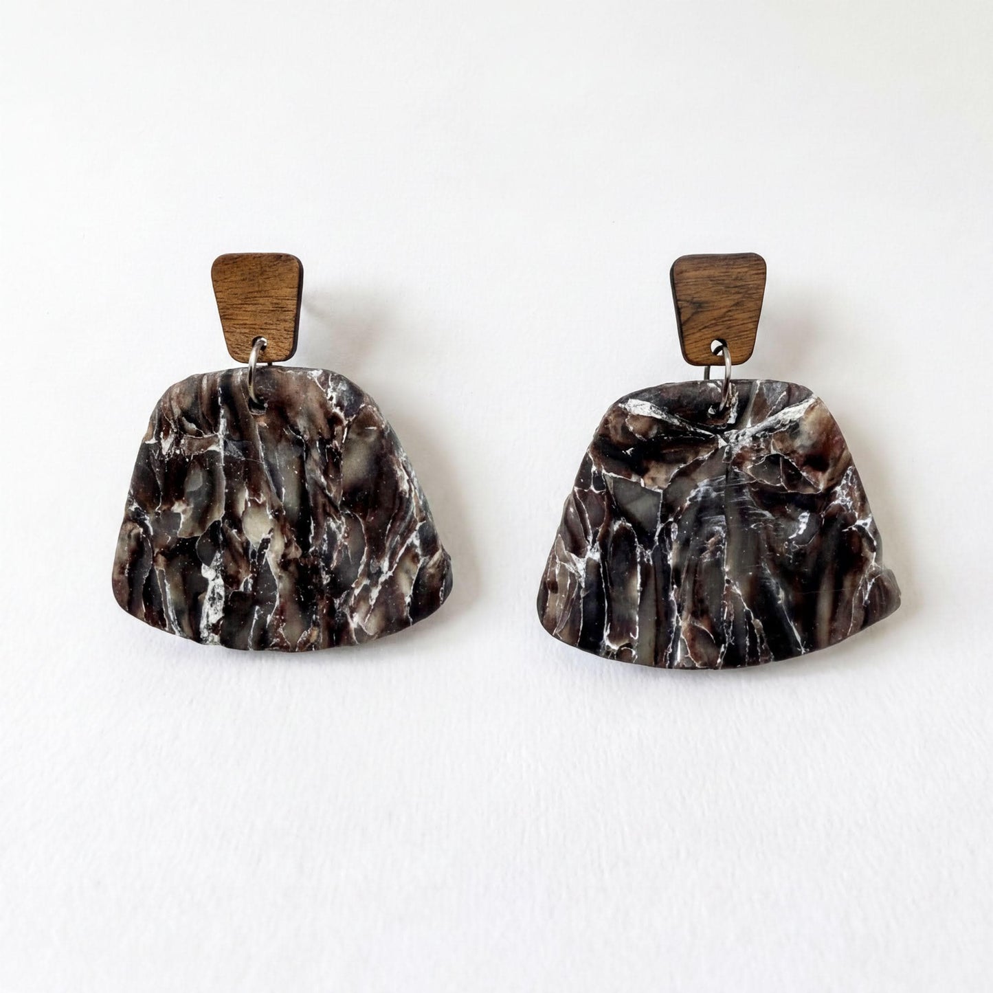 A pair of earrings with a marble-like texture and wooden accents, displayed against a white background.