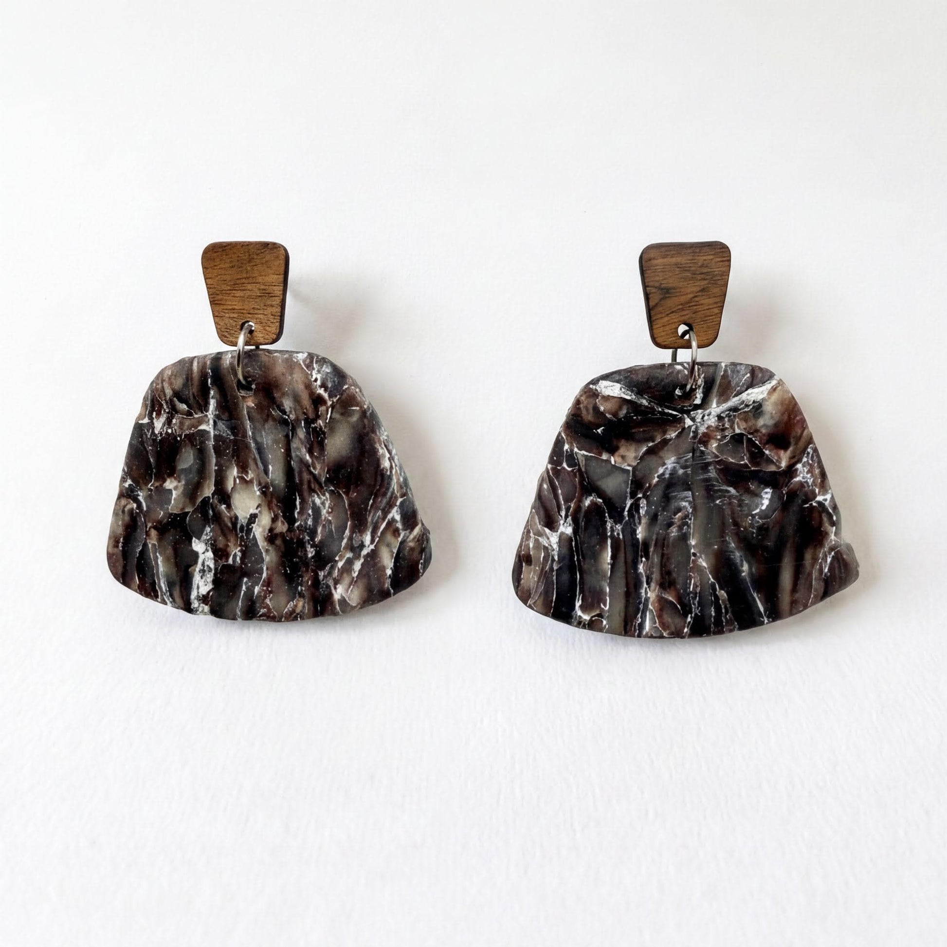 A pair of earrings with a marble-like texture and wooden accents, displayed against a white background.