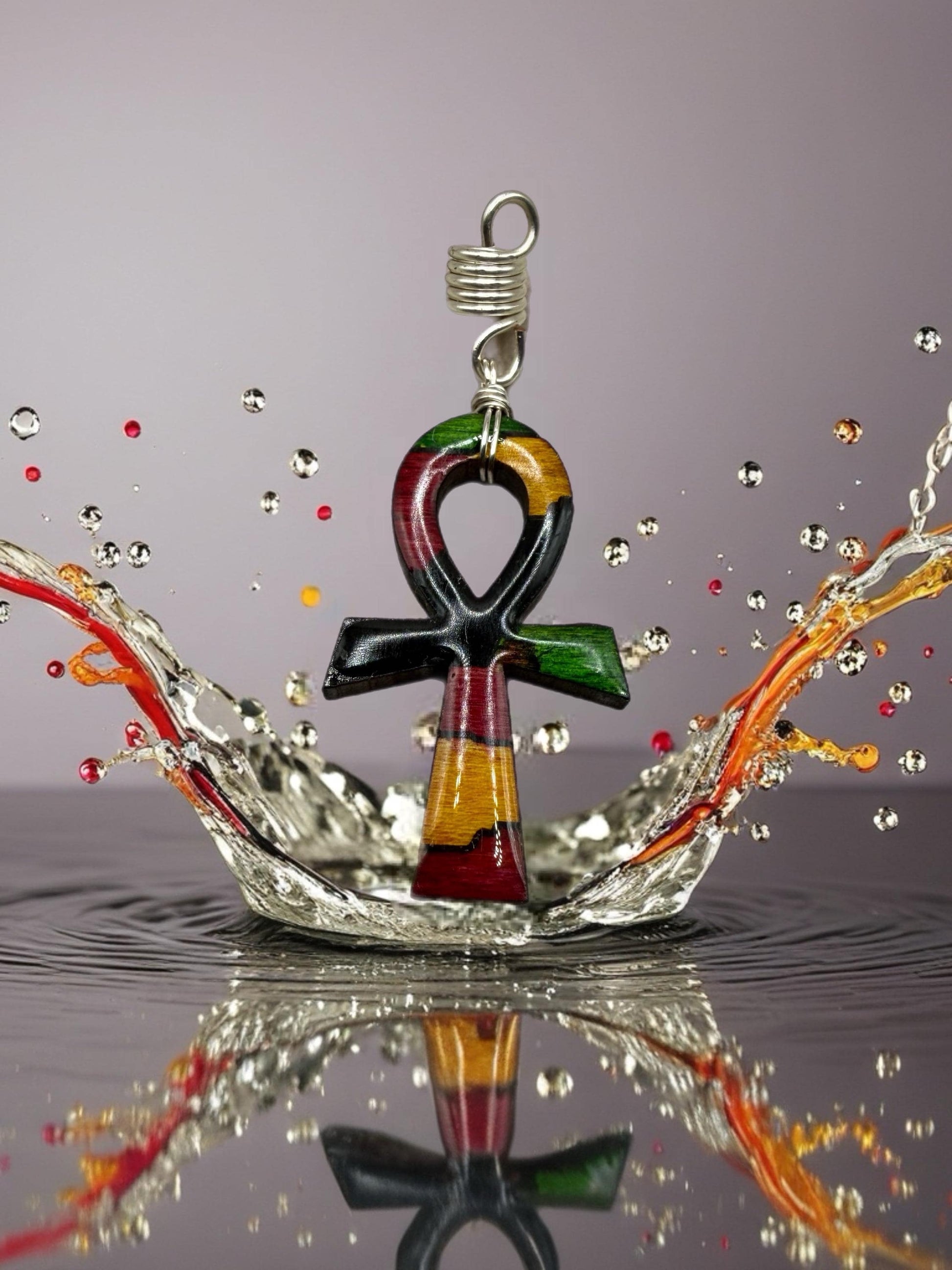 a colorful pendant with a cross-shaped design, surrounded by splashes of water and reflections on a surface.