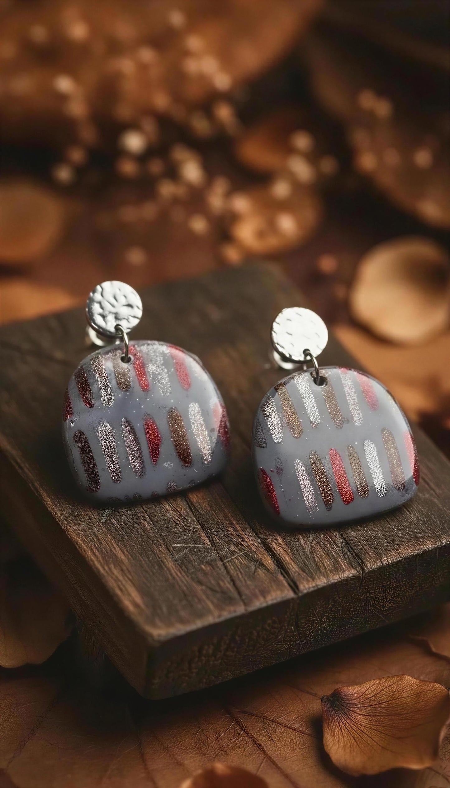 a pair of earrings with a metallic design, placed on a wooden surface.