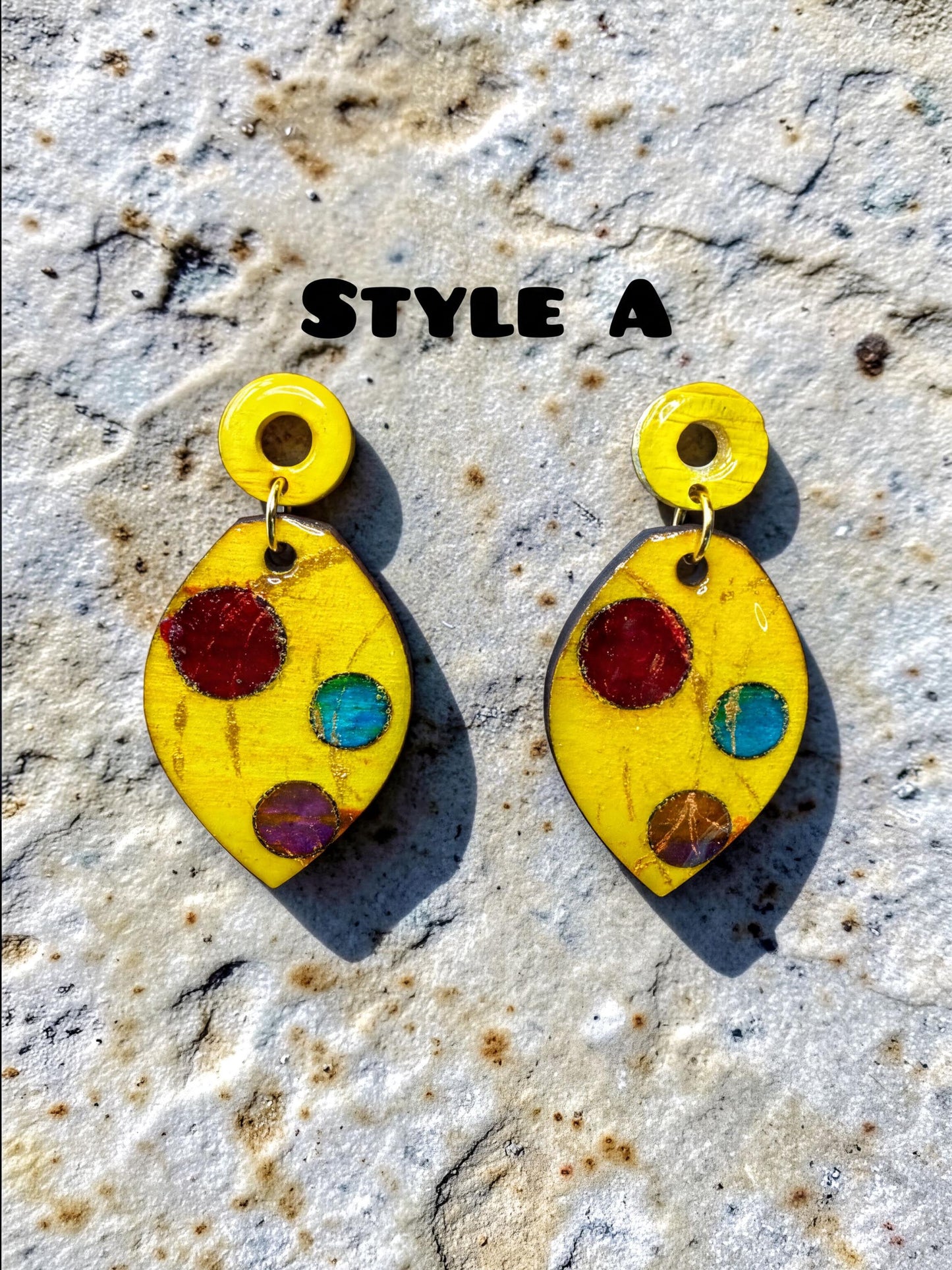 a pair of yellow earrings with colorful polka dots, displayed on a textured surface.