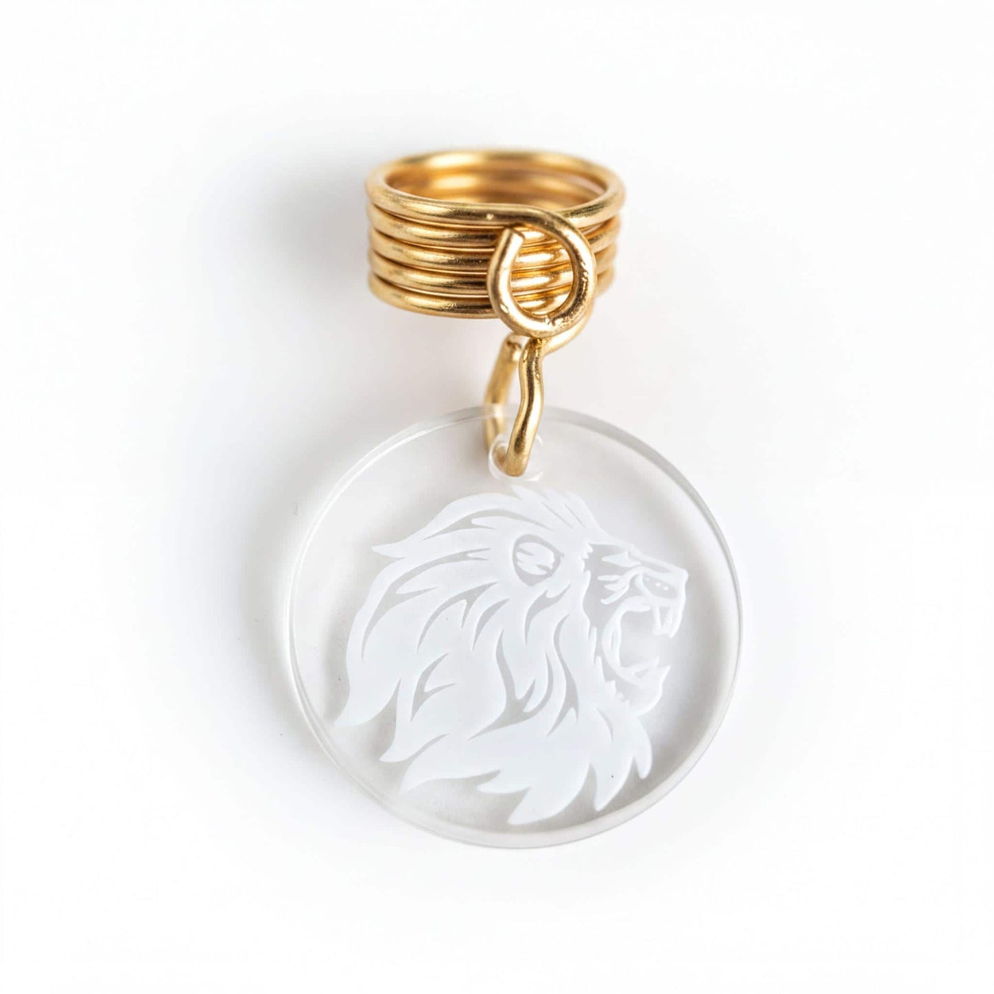 a clear pendant with a white lion's head design, and it is attached to a gold ring.