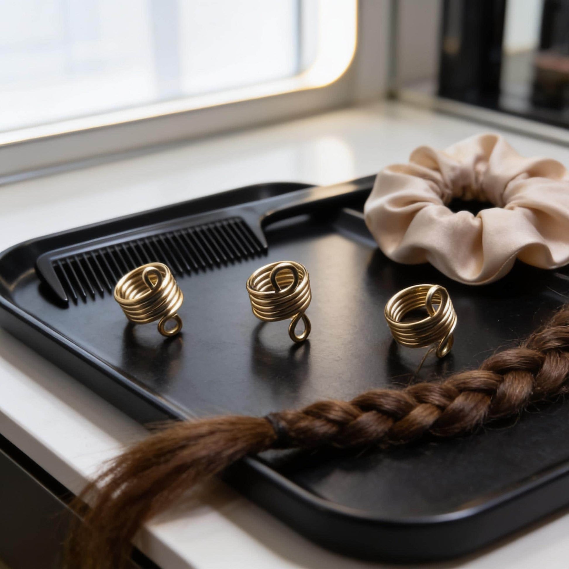 A black tray with three gold spiral hair accessories, a white scrunchie, and a braided hair accessory, all placed on a white surface.