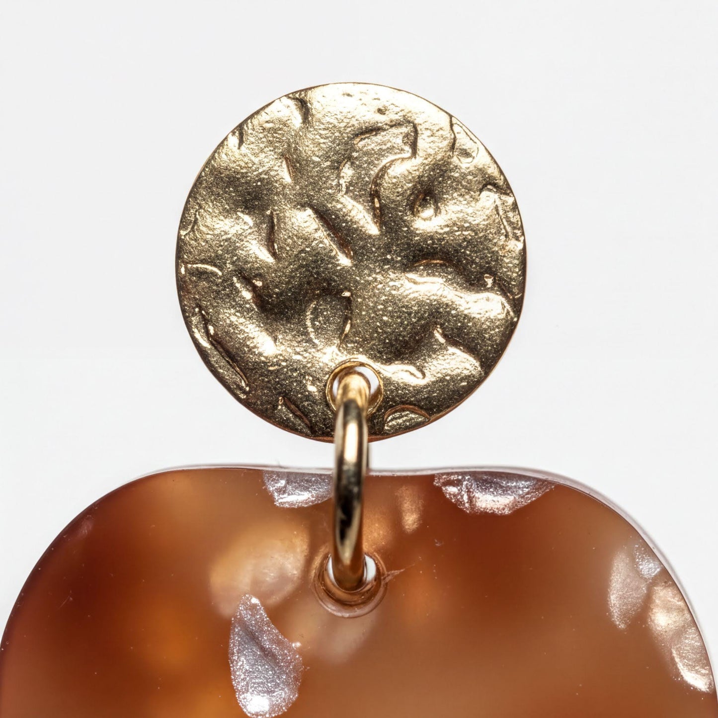 A close-up view of a gold-colored metal earring with a circular design on top, attached to a brown-colored, textured surface.