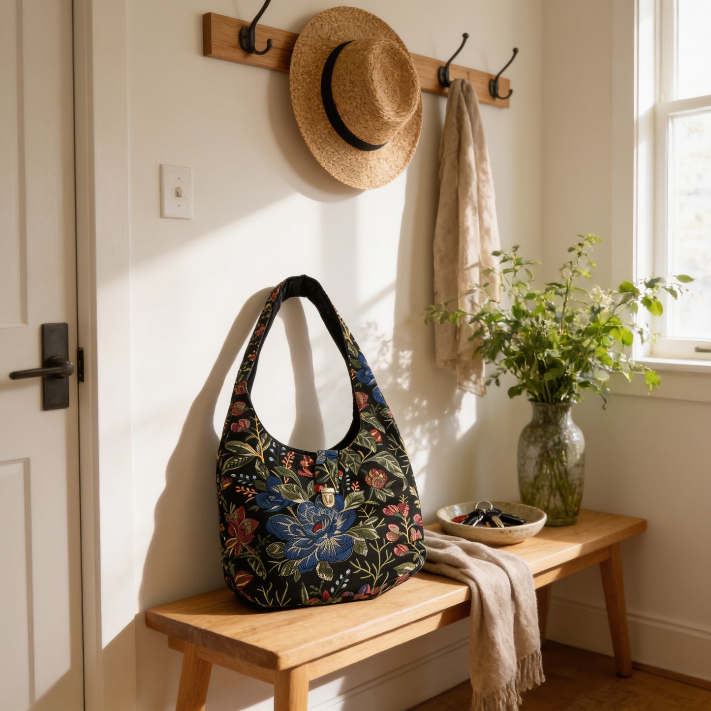 A wooden bench with a floral patterned purse, a hat rack, a vase of greenery, and a bowl of keys on it.