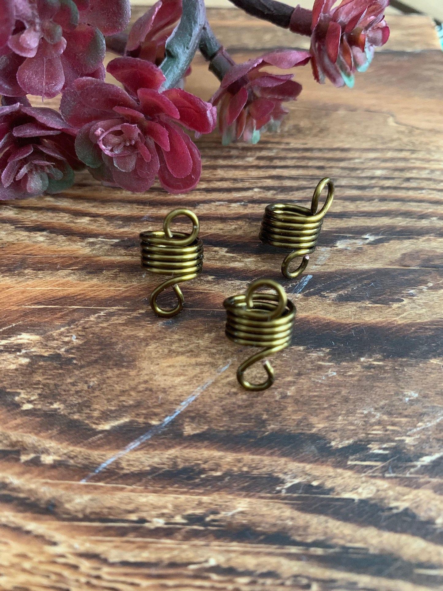three brass hair clips arranged on a wooden surface, with a backdrop of red flowers.