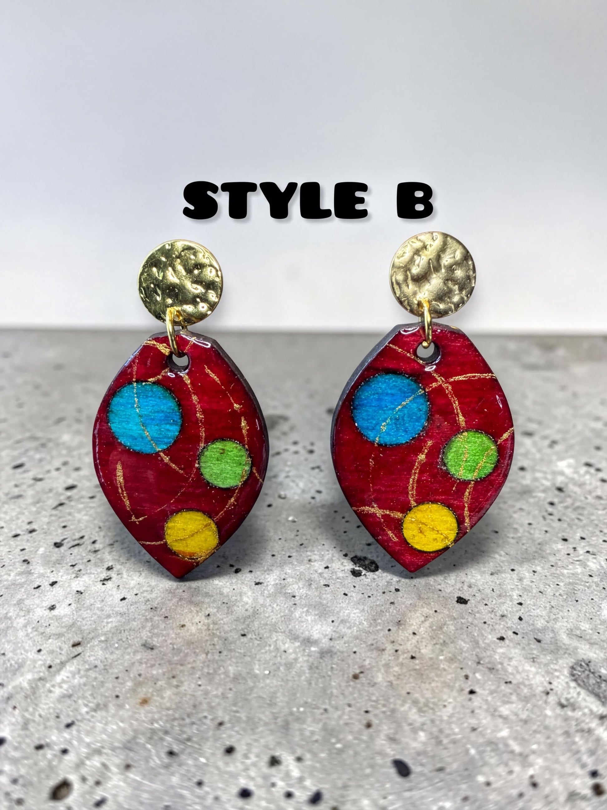 a pair of red earrings with colorful polka dots, displayed on a speckled surface.