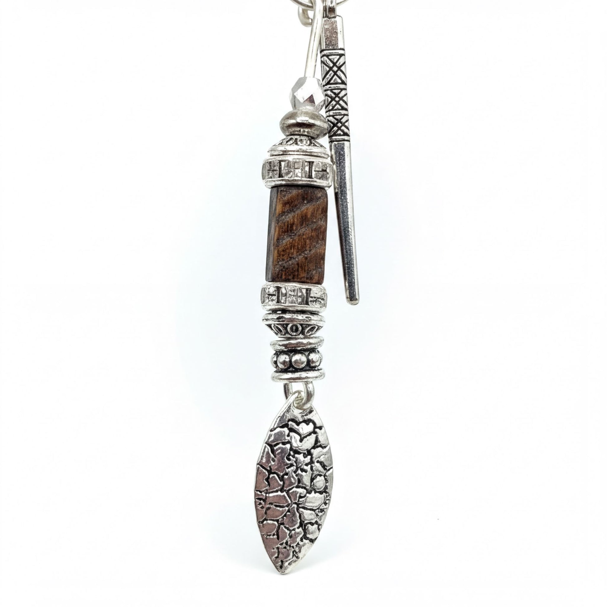 A silver necklace with a pendant featuring a combination of metal and wood elements, including a rectangular metal piece, a curved metal piece, and a leaf-like metal piece.