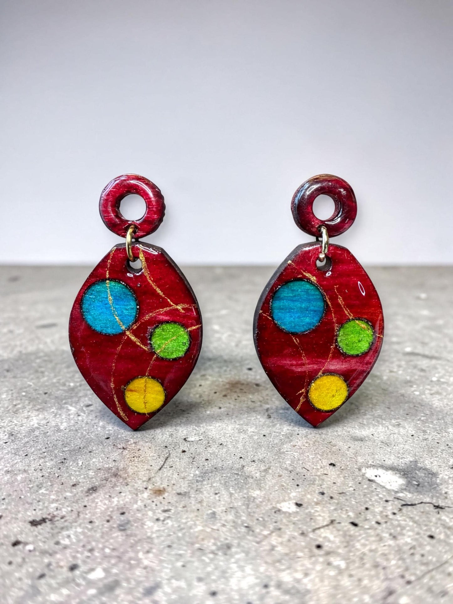 A pair of red earrings with colorful polka dot designs on a gray surface.