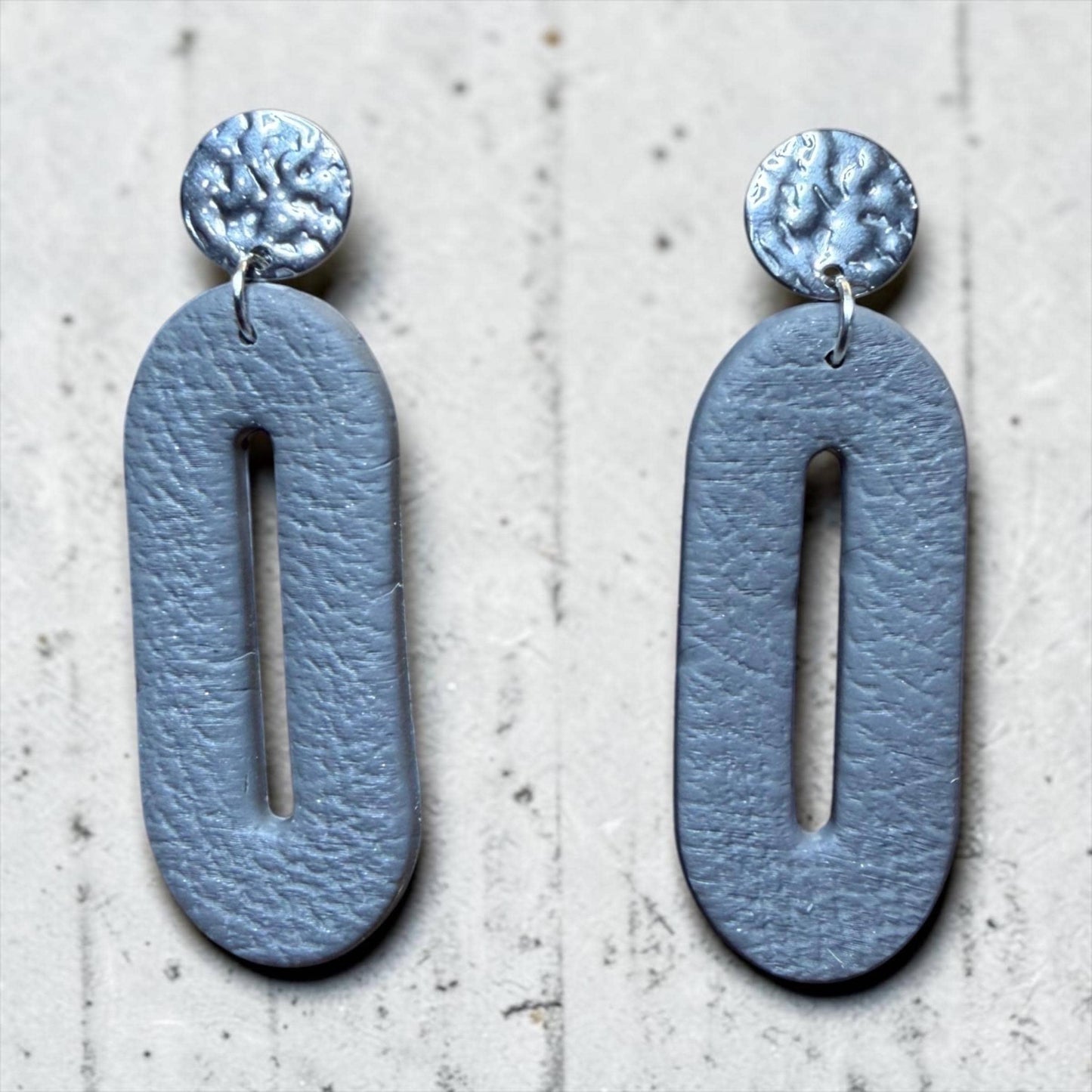 A pair of gray leather earrings with a circular cutout in the middle.