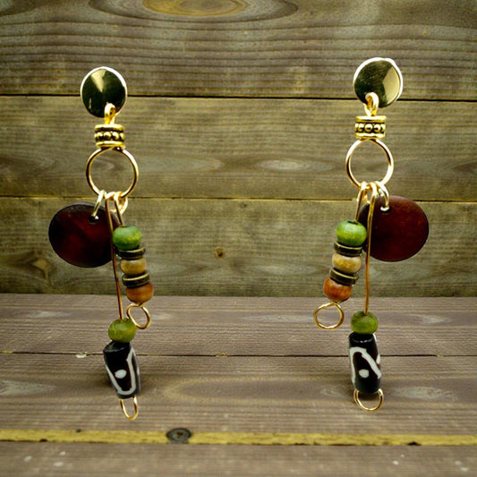 A pair of gold earrings with colorful beads and a circular pendant, displayed on a wooden surface.