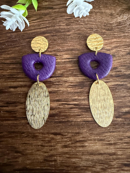 a pair of earrings with a combination of purple and gold colors, placed on a wooden surface.